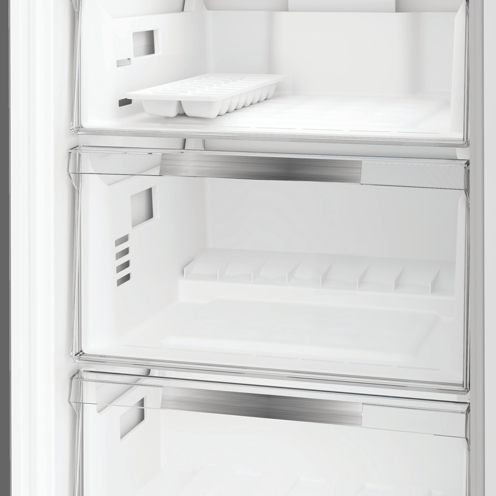 Im Inneren eines weißen Kühlschranks, der Regale und Schubladen zeigt. In der oberen Kammer befindet sich eine Eiswürfelschale. Der Kühlschrank ist leer.