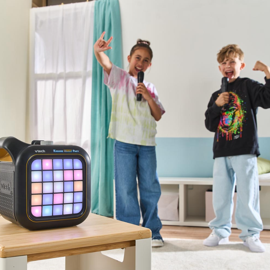 Zwei Kinder singen Karaoke mit Mikrofonen. Ein Lautsprecher steht auf einem Tisch. Ein Kind gestikuliert, das andere posiert.