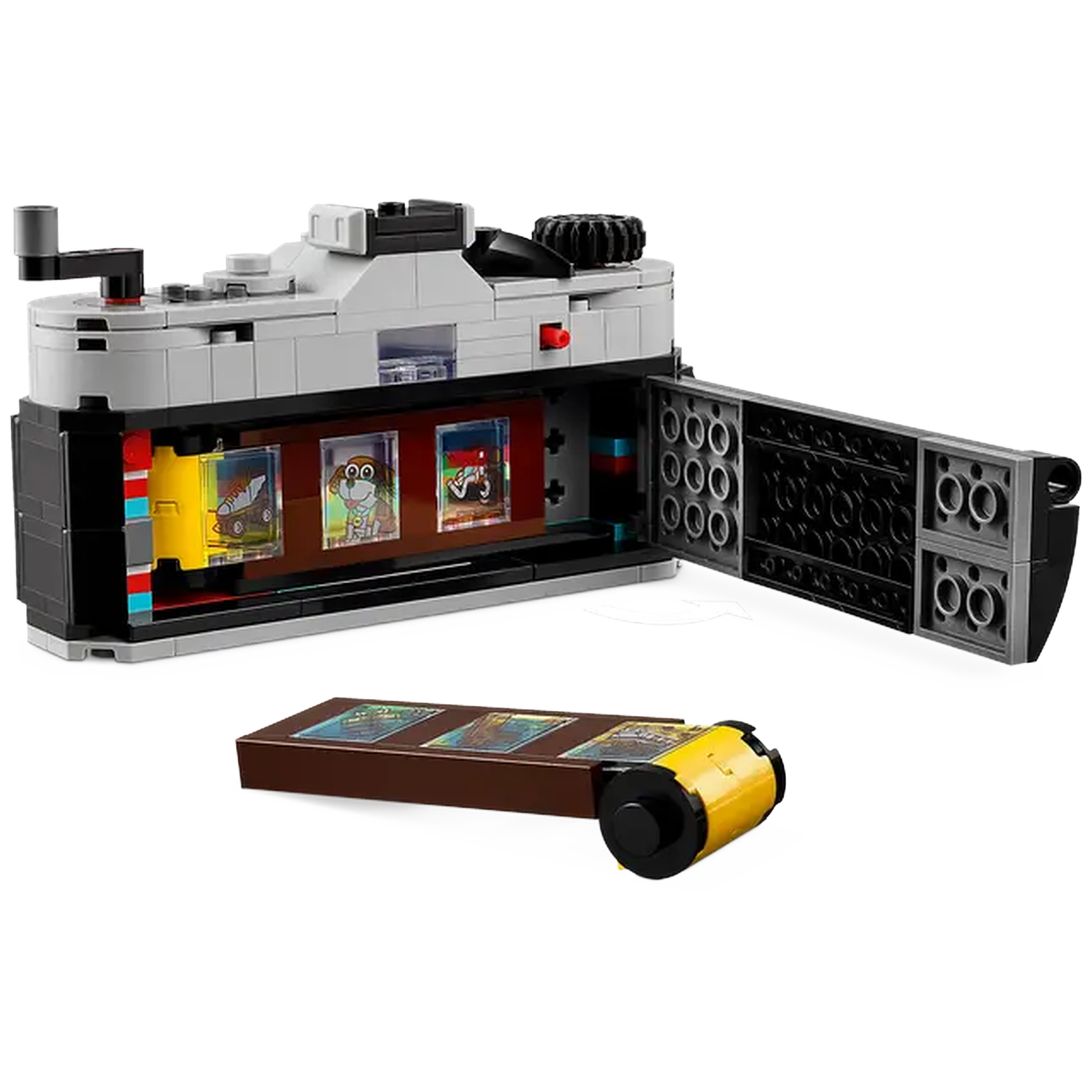 A Lego camera with an open back, showing film strips with cartoon images. A film roll and a box of film strips are on the table.