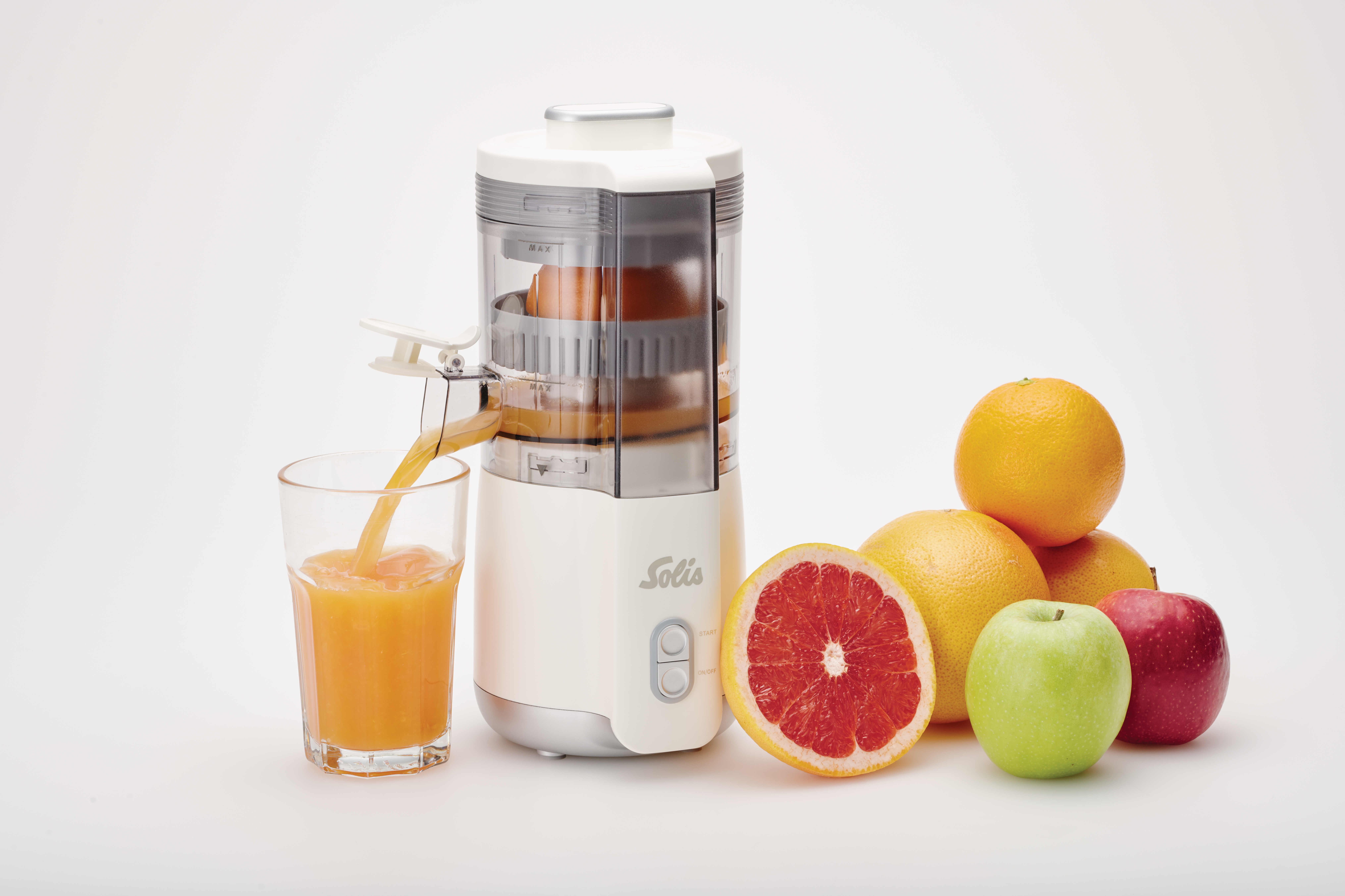 Entsafter gießt Saft in ein Glas. Orangen, Grapefruit und Äpfel stehen neben dem Entsafter auf einer weißen Oberfläche.