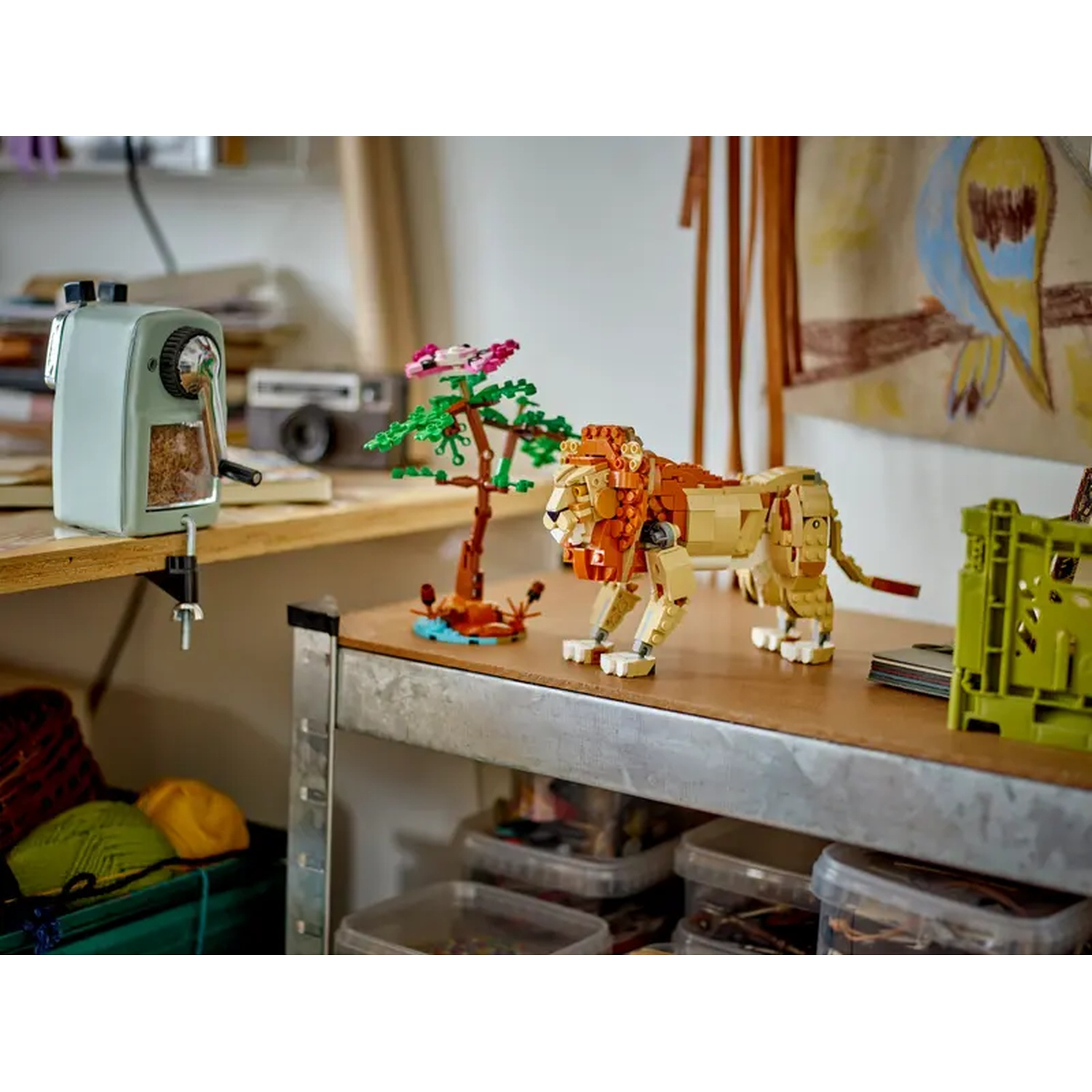 A Lego lion stands on a wooden surface next to a tree and a pencil sharpener. Background has a drawing of a bird.