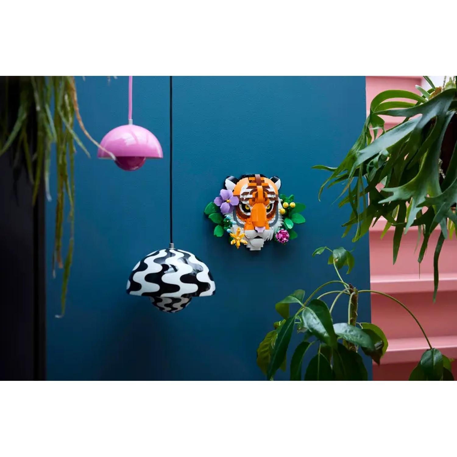A Lego tiger head with a floral wreath on a blue wall, two lamps, and plants.