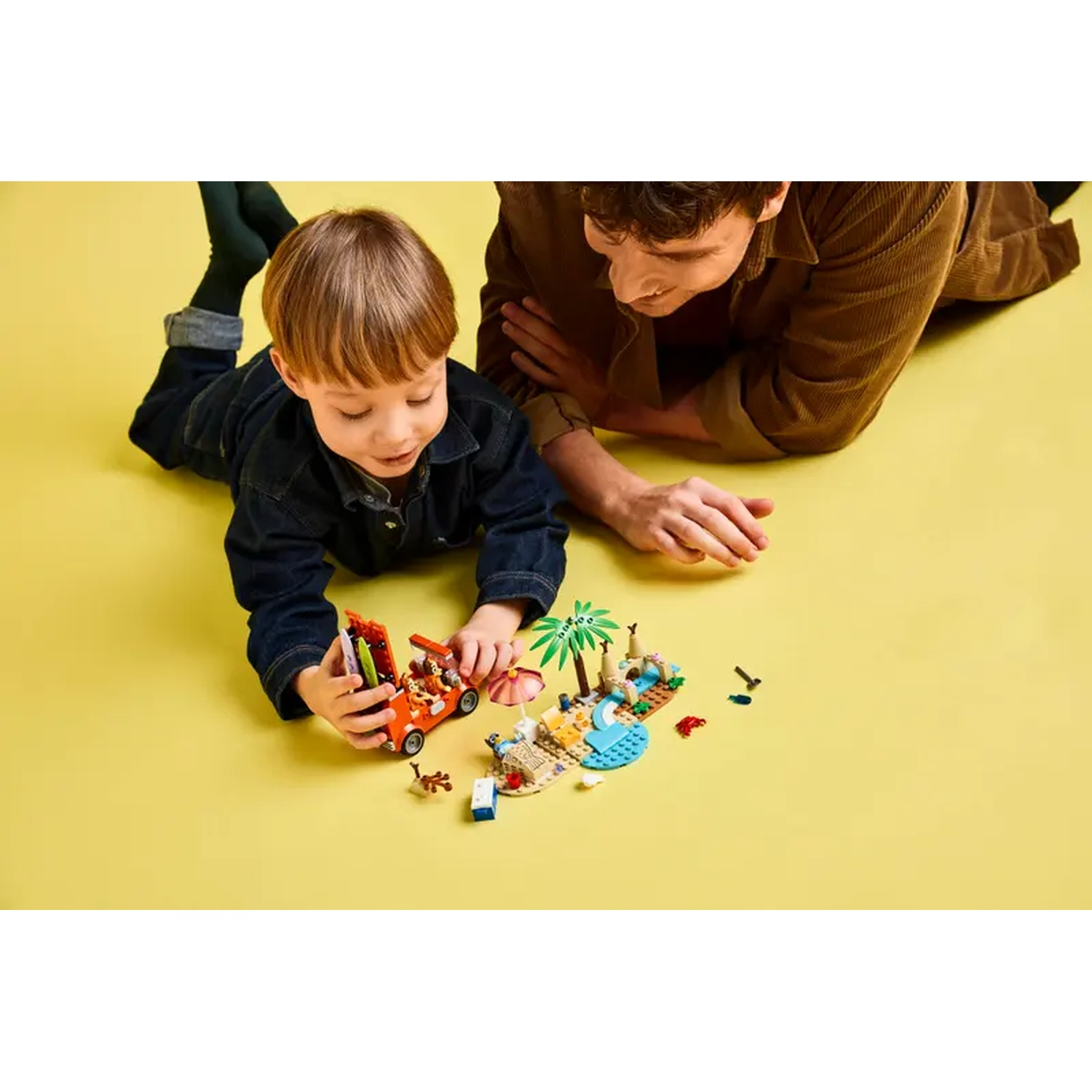 Een kind en een volwassene spelen met Lego. Het kind concentreert zich op een oranje auto, de volwassene kijkt ook naar het speelgoed.