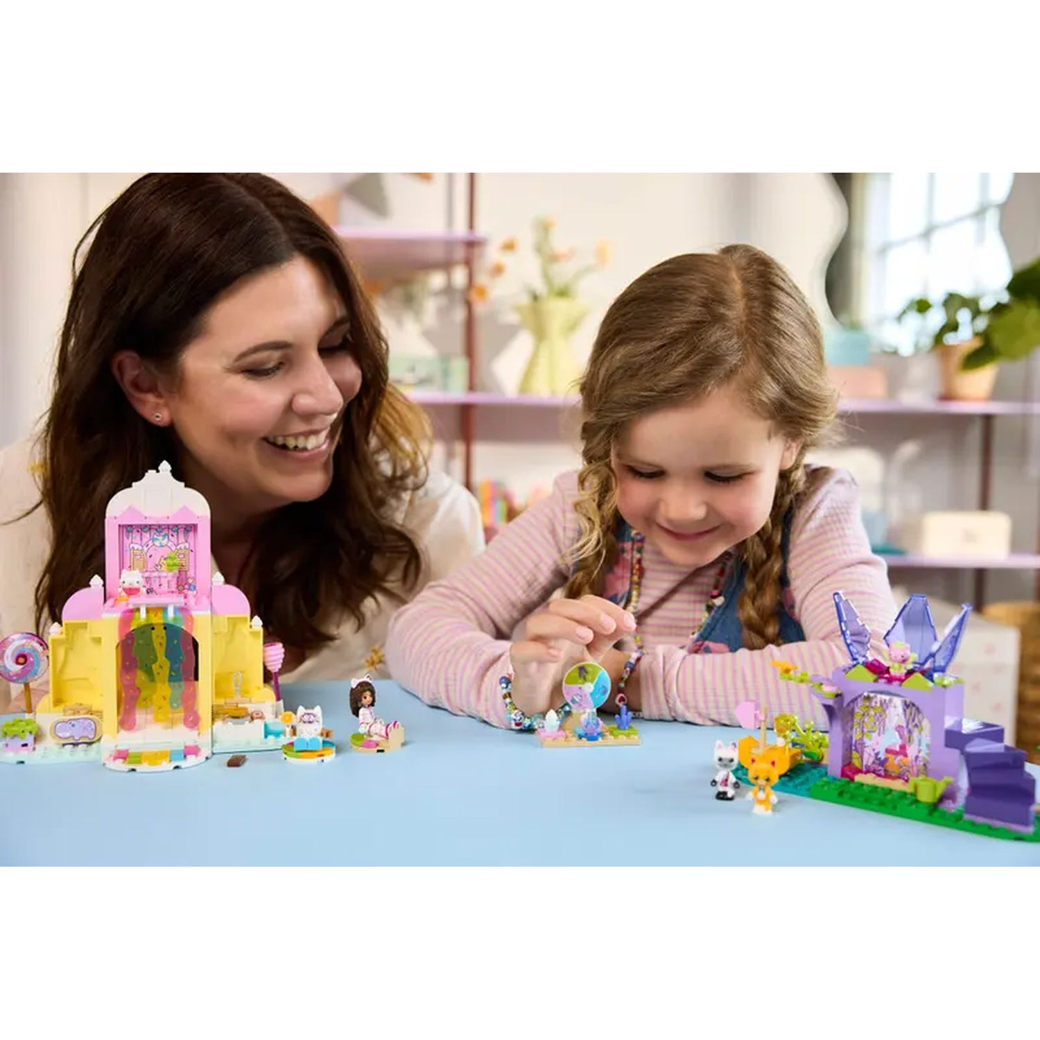 Une femme et une fille jouent avec des châteaux jouets. La scène comprend des jeux de jouets colorés et des figurines sur une table bleue.
