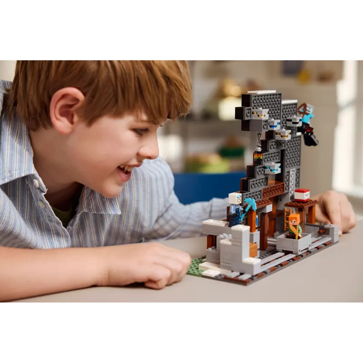Un garçon sourit devant un jeu Lego Minecraft. L'ensemble montre une mine avec des figurines, de la TNT et un wagon sur rails.