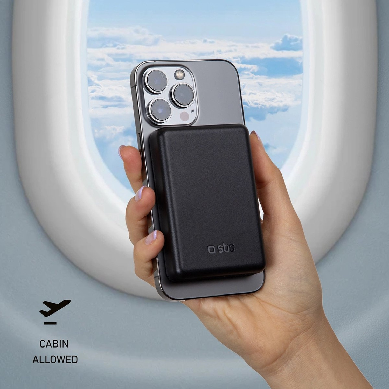 Une main tenant un téléphone avec un chargeur noir, devant une fenêtre d'avion montrant des nuages. Icône cabine autorisée.