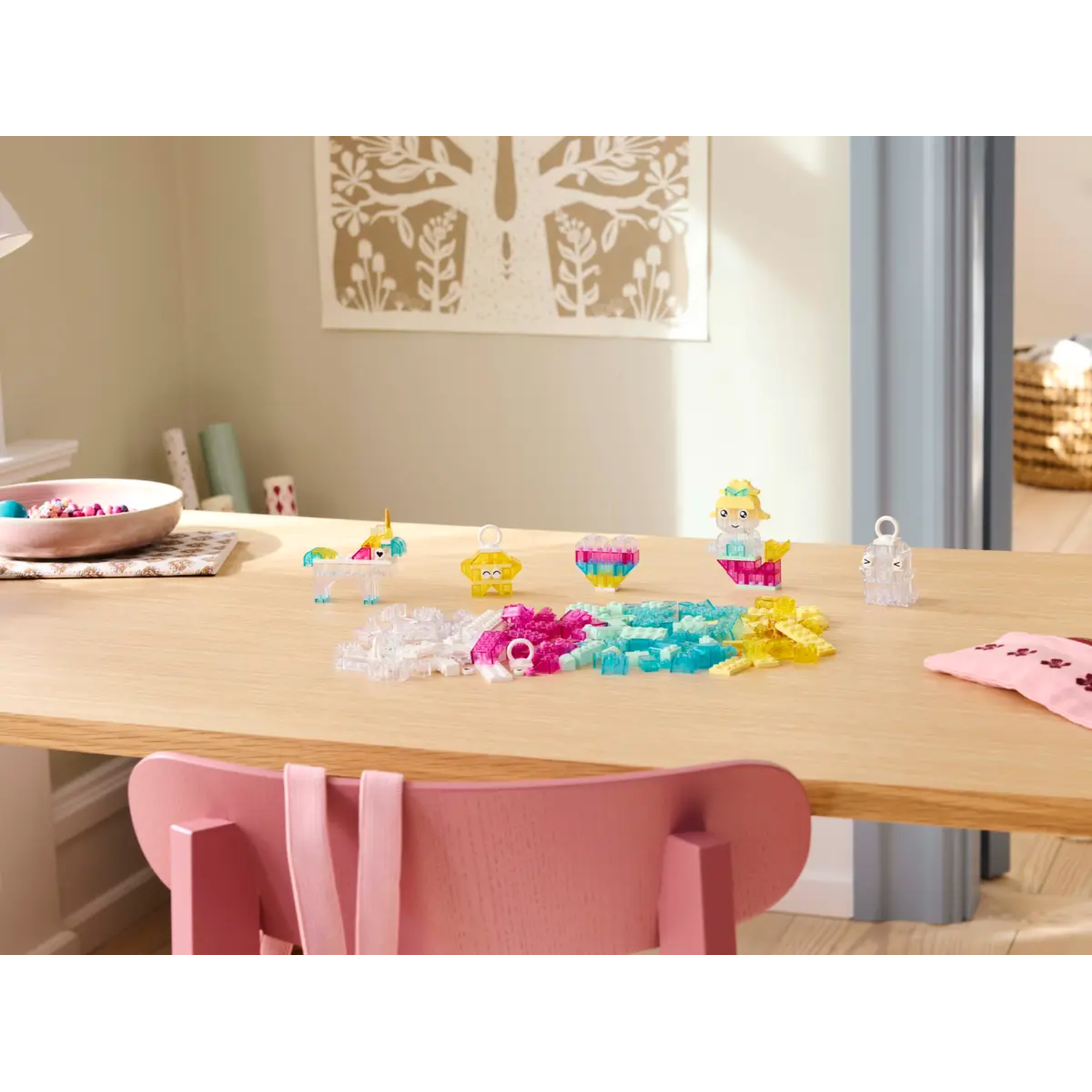Een houten tafel met kleurrijke speelgoedblokken en figuren. Een roze stoel staat op de voorgrond. Een kom met kralen staat op tafel.