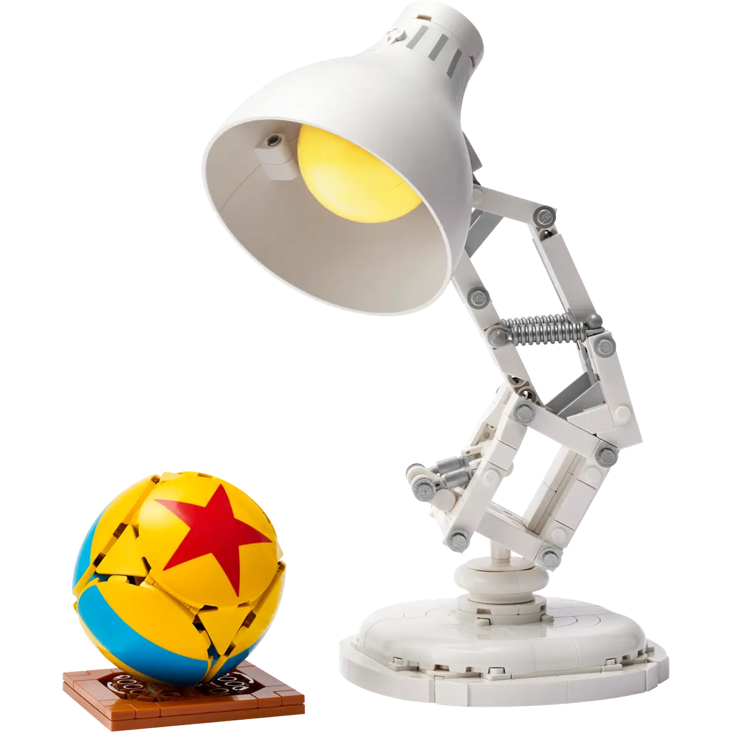 A white desk lamp and a yellow, blue, and red ball are on a white surface. The lamp is lit. The ball has a red star.