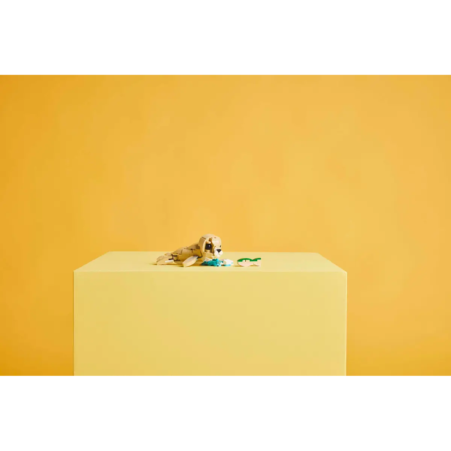 A Lego seal toy sits on a yellow cube. The background is a solid yellow. The seal is light brown with black eyes.