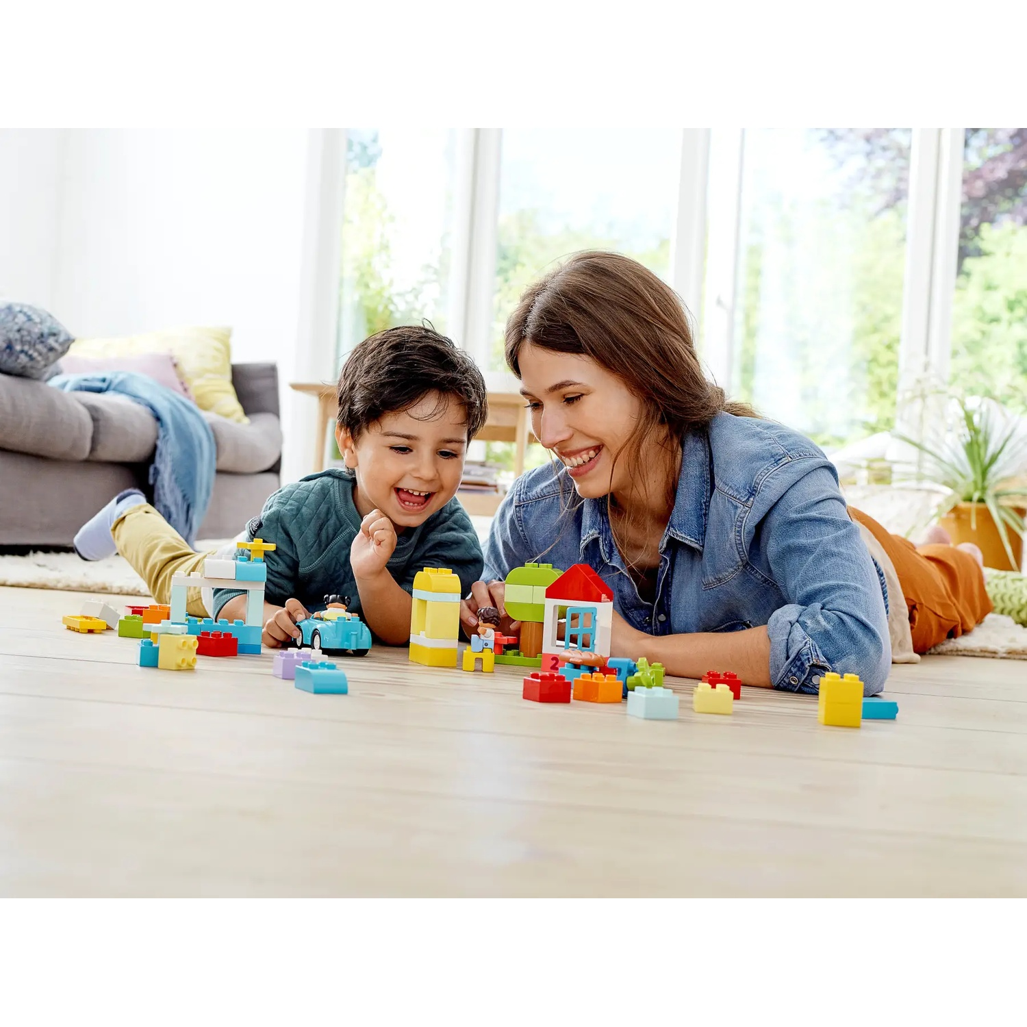 Une femme et un enfant sont allongés sur le sol, jouant avec des blocs de construction colorés. Ils sourient.