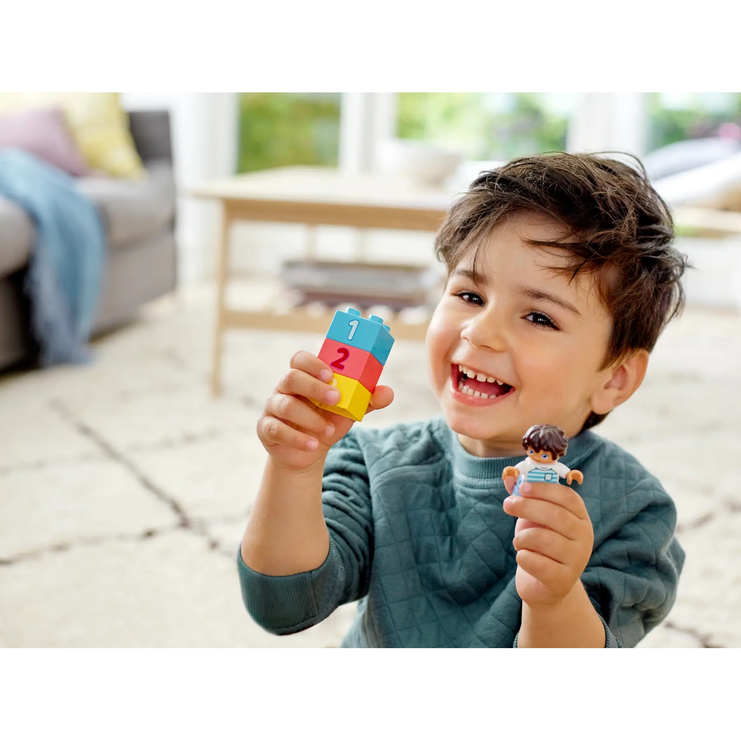 Un garçon souriant tient des blocs de construction et une figurine. Les blocs sont numérotés et la figurine est une petite poupée.