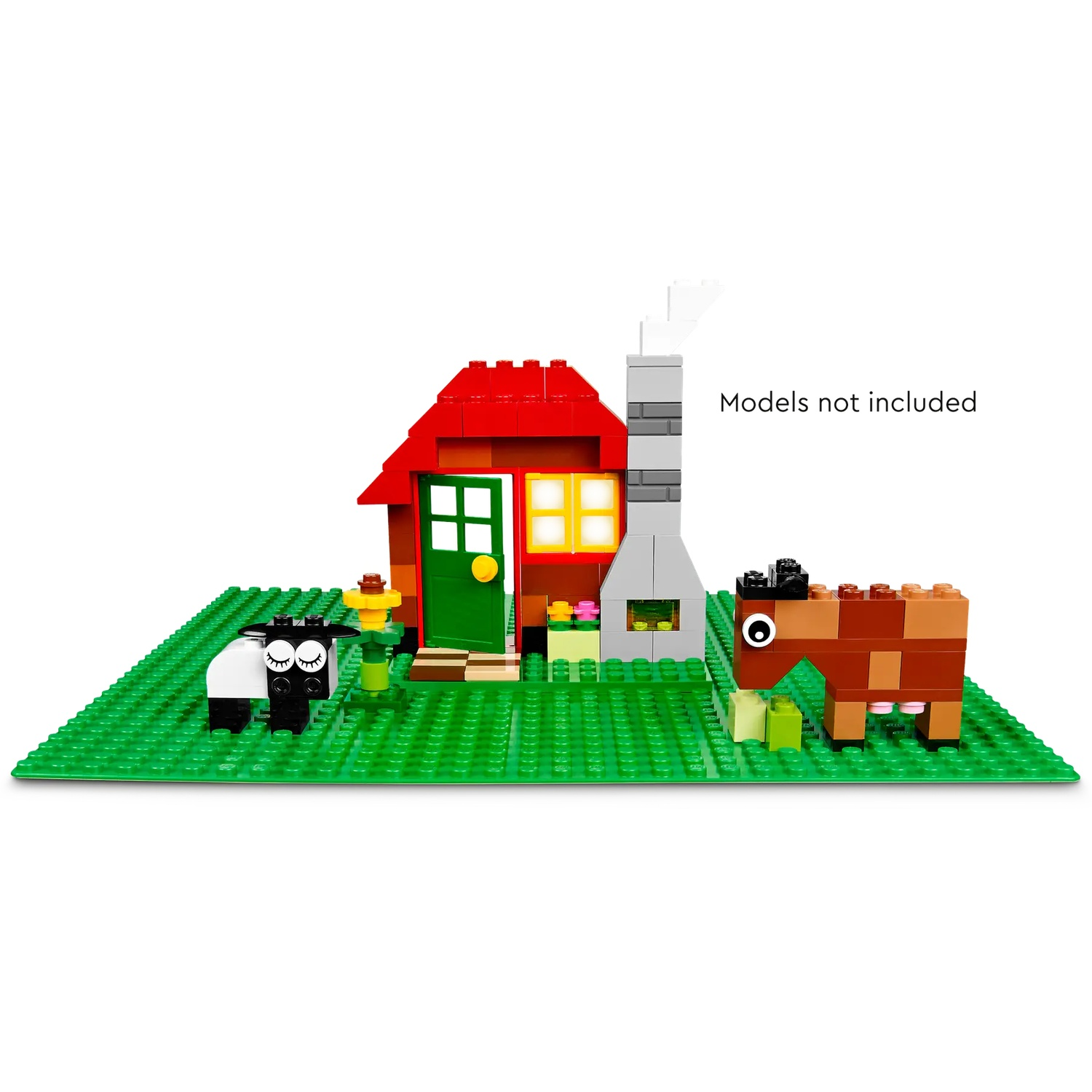 Une scène de ferme Lego avec une maison rouge, une cheminée, un mouton et une vache sur une plaque de base verte. Modèles non inclus.