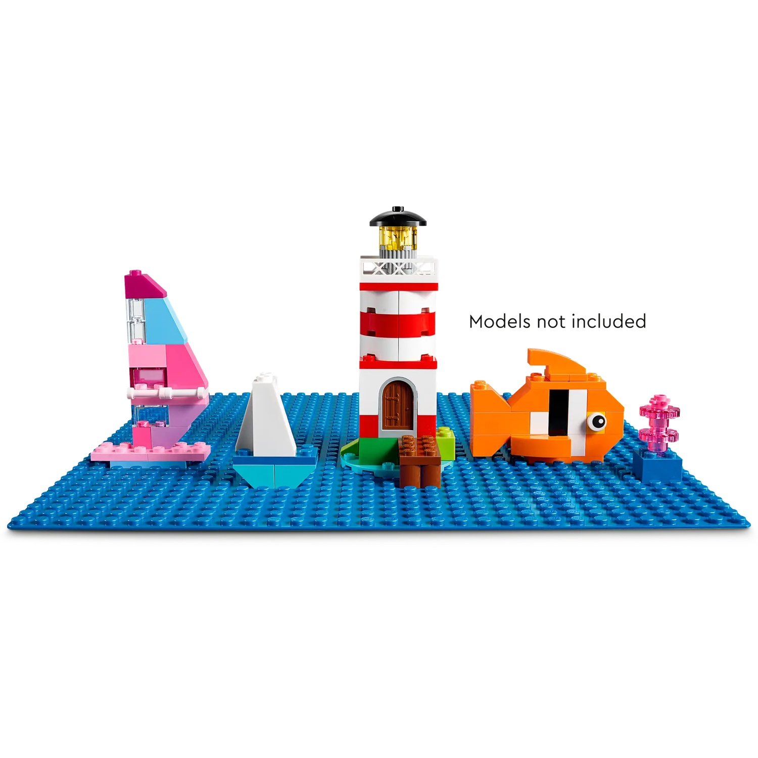 Scène Lego sur base bleue. Comprend un phare, un voilier, un poisson et d'autres structures. Texte 'Modèles non inclus' présent.