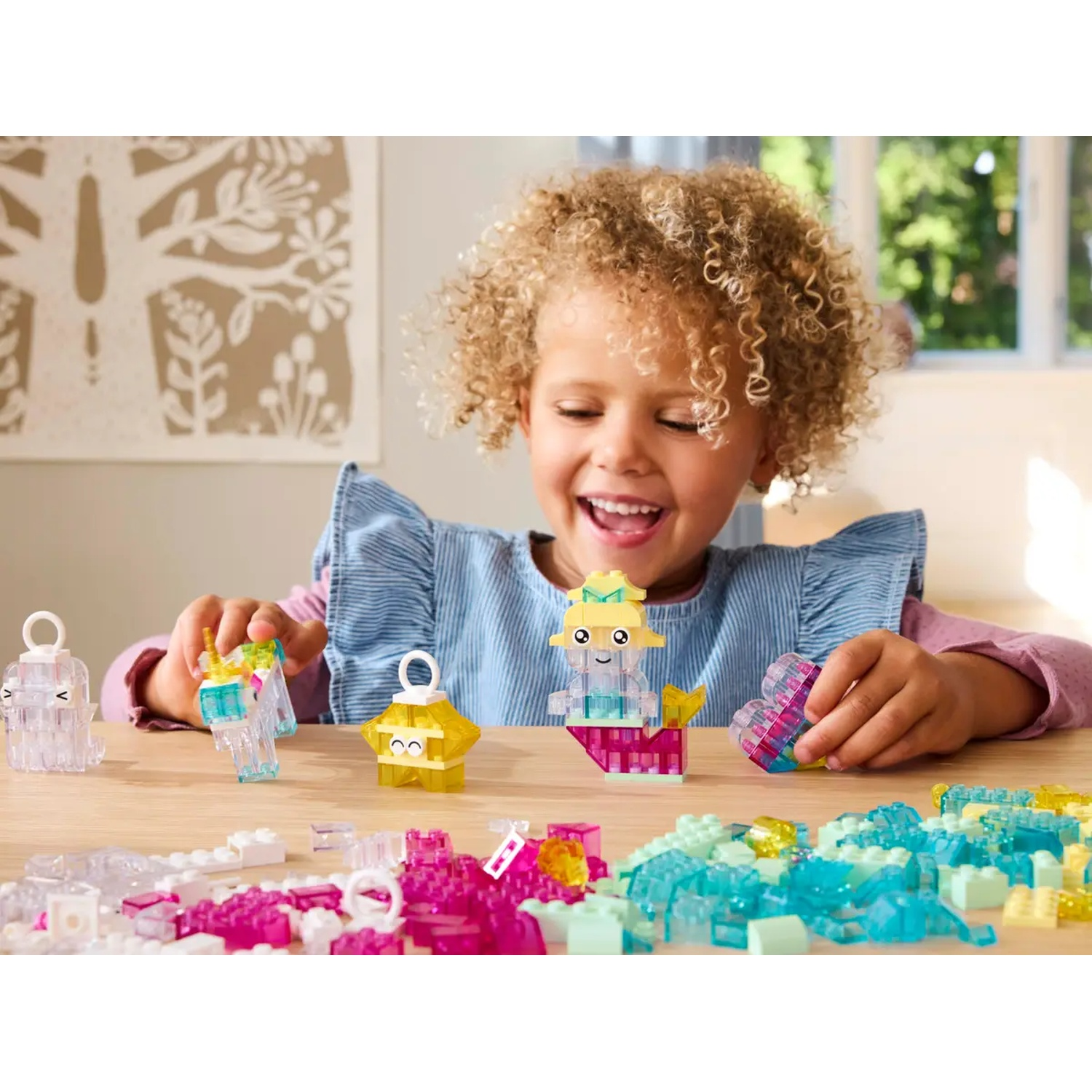 Une fillette souriante joue avec des blocs de construction colorés. Plusieurs figurines en blocs sont sur la table. D'autres blocs sont dispersés.