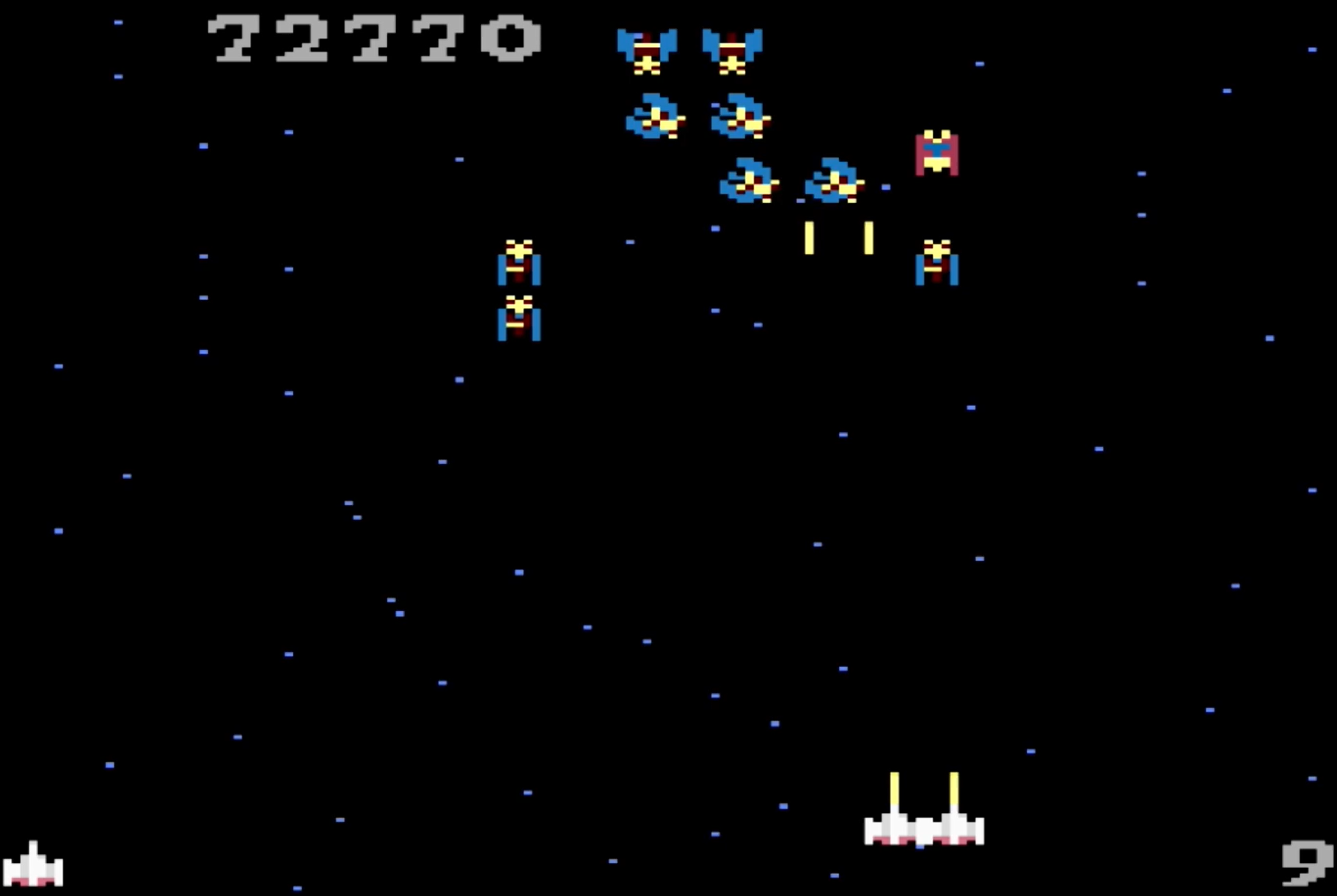 Un écran de jeu de tir spatial rétro. Des vaisseaux spatiaux et des ennemis dans l'espace. Le score est de 72770. Le vaisseau du joueur en bas et a 9 vies.