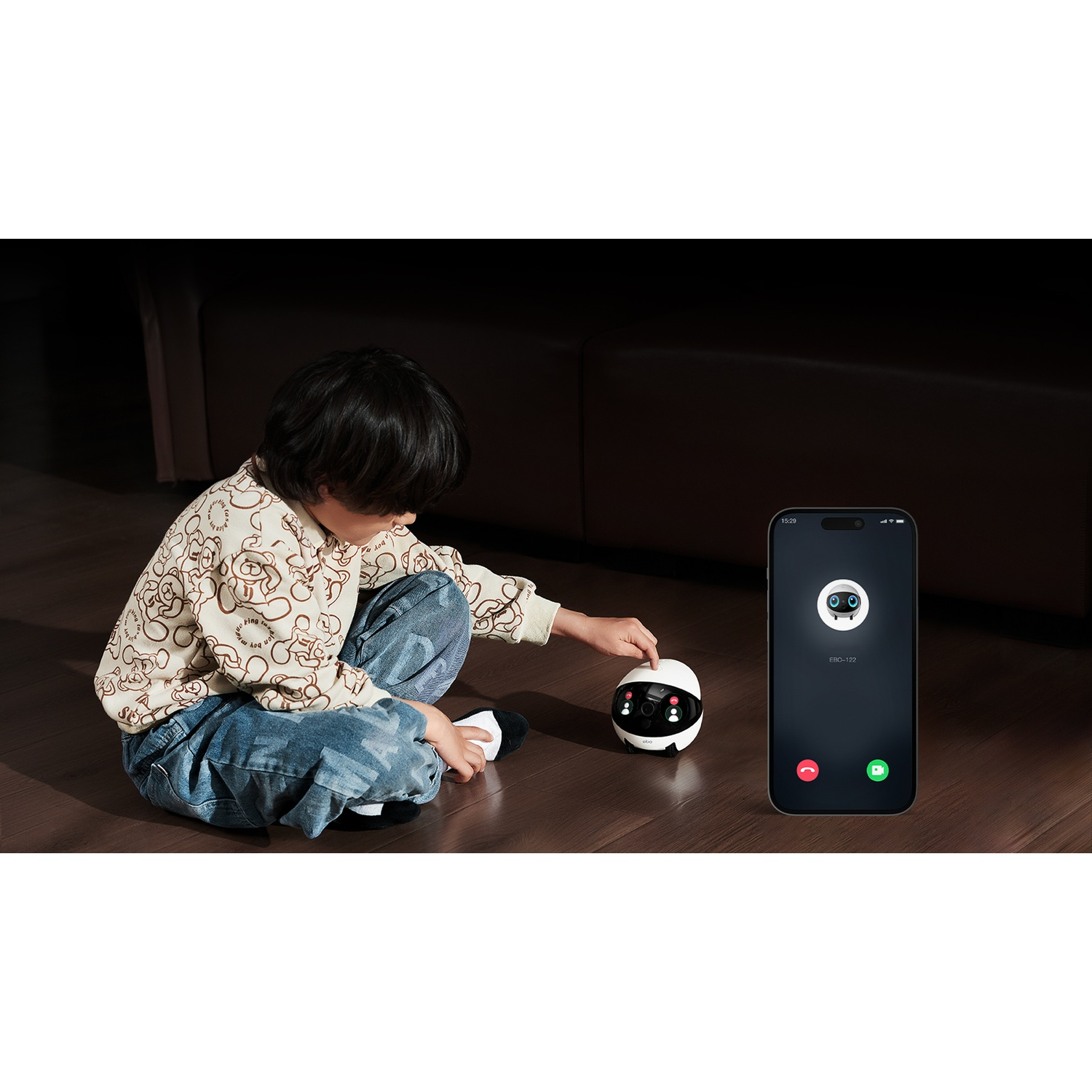 Un bambino interagisce con un robot. Un telefono mostra una chiamata dal robot. Il bambino indossa una camicia fantasia e jeans.