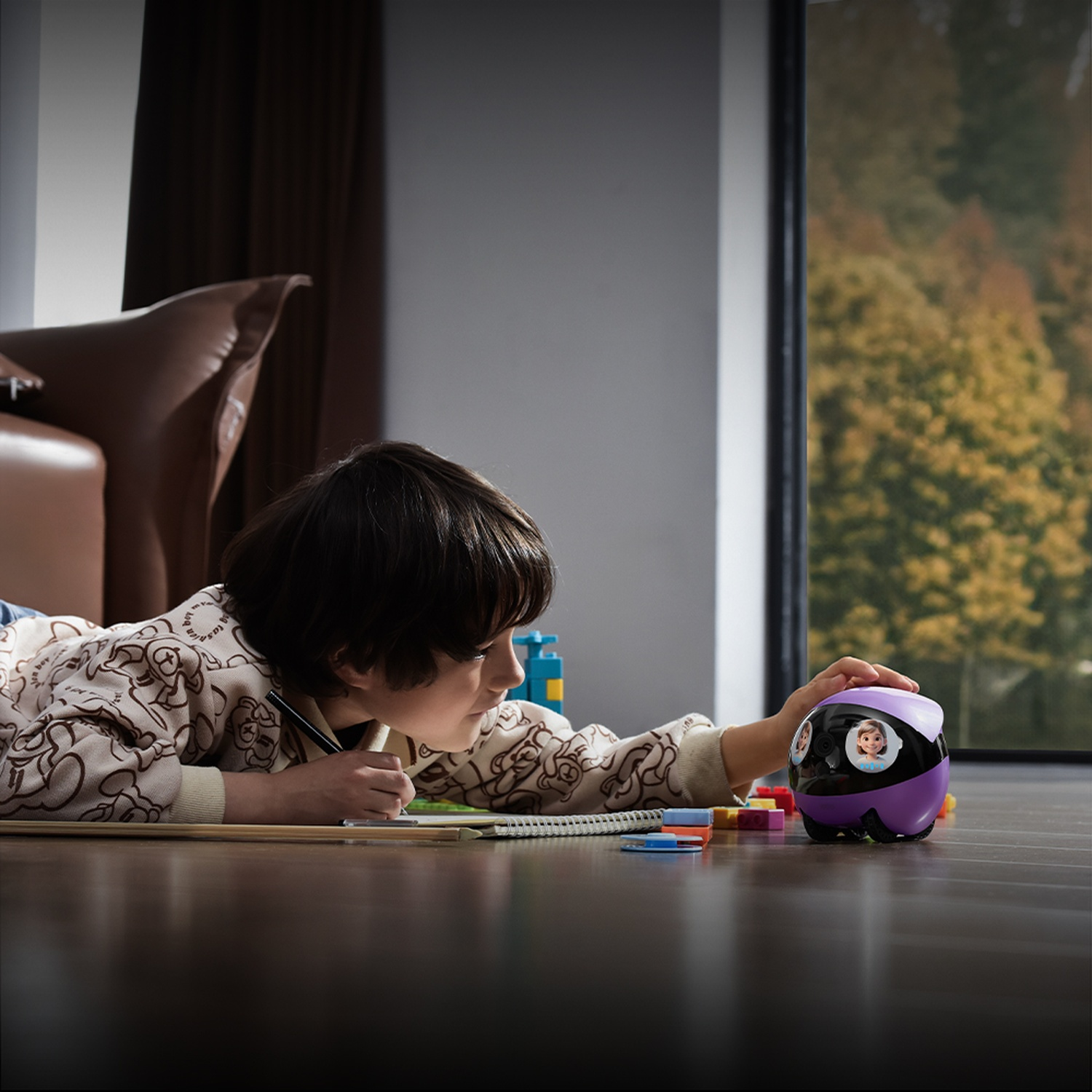 Un bambino disegna sul pavimento accanto a un robot viola e nero. Una finestra mostra alberi. Dietro il bambino c'è un divano marrone.