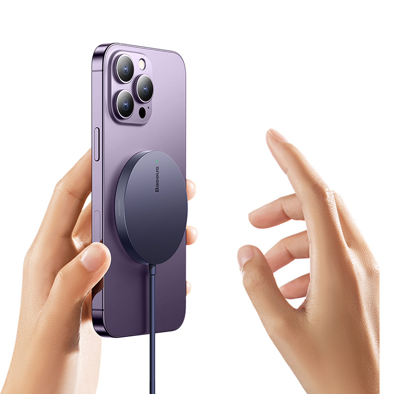 Una persona sostiene un teléfono morado con un cargador inalámbrico adjunto. Otra mano se extiende. Fondo blanco.