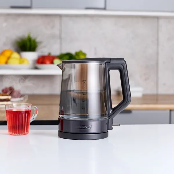 Szklany czajnik z wodą, filiżanka czerwonej herbaty i półka z owocami stoją na białym blacie.