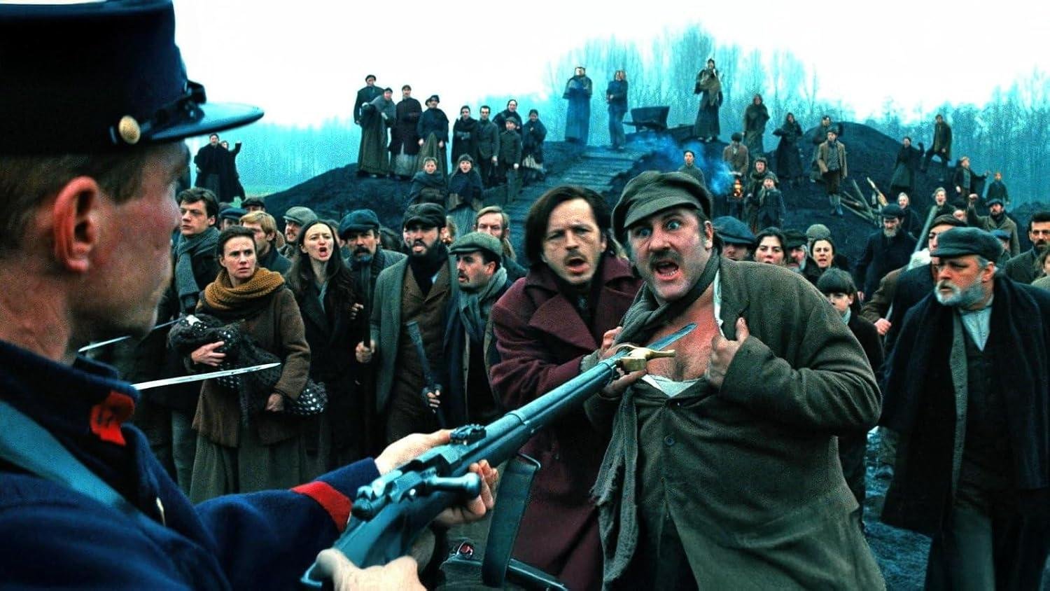 Ein Soldat zielt mit einem Gewehr auf eine Menschenmenge. Ein Mann hält ein Messer. Andere schauen ängstlich zu. Eine historische Szene.