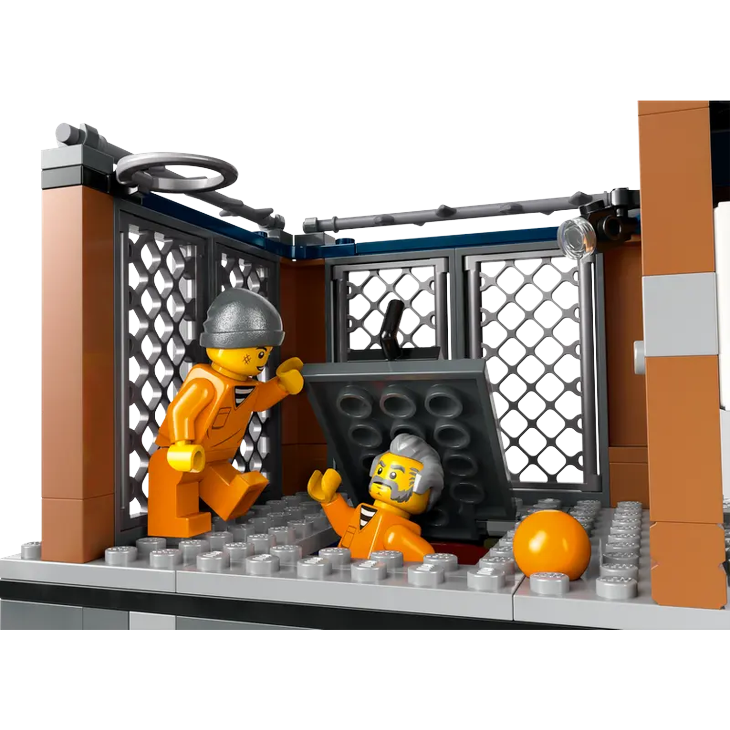 Lego jail scene. Two Lego figures in orange jumpsuits, one opens a cell door, another lies on the ground, and an orange ball.