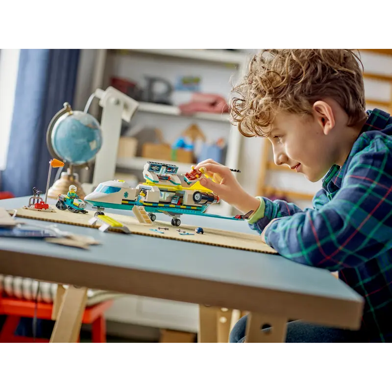 A boy plays with a Lego airplane set. The set includes a small plane, a motorcycle, and other accessories on a table.