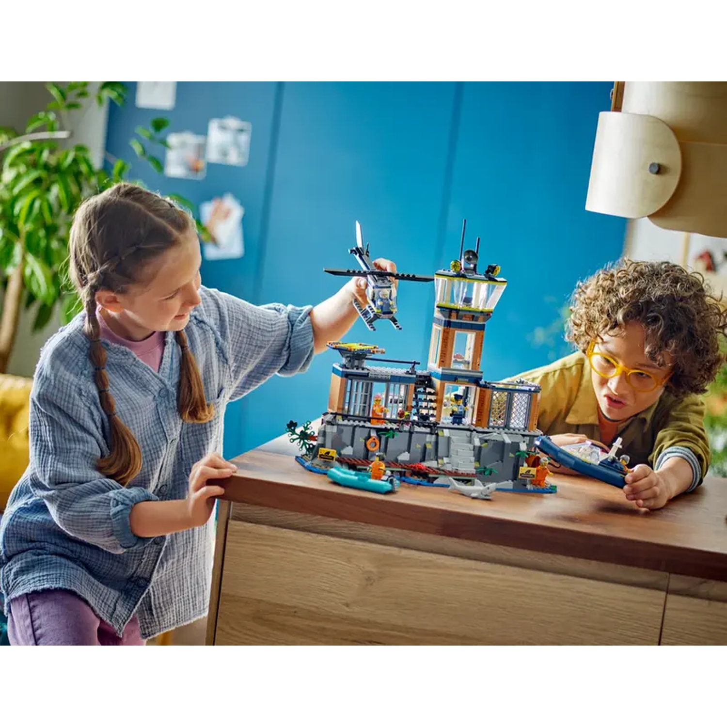 Deux enfants jouent avec un ensemble Lego. L'ensemble est un poste de police. Un enfant tient un hélicoptère. L'autre tient un bateau.