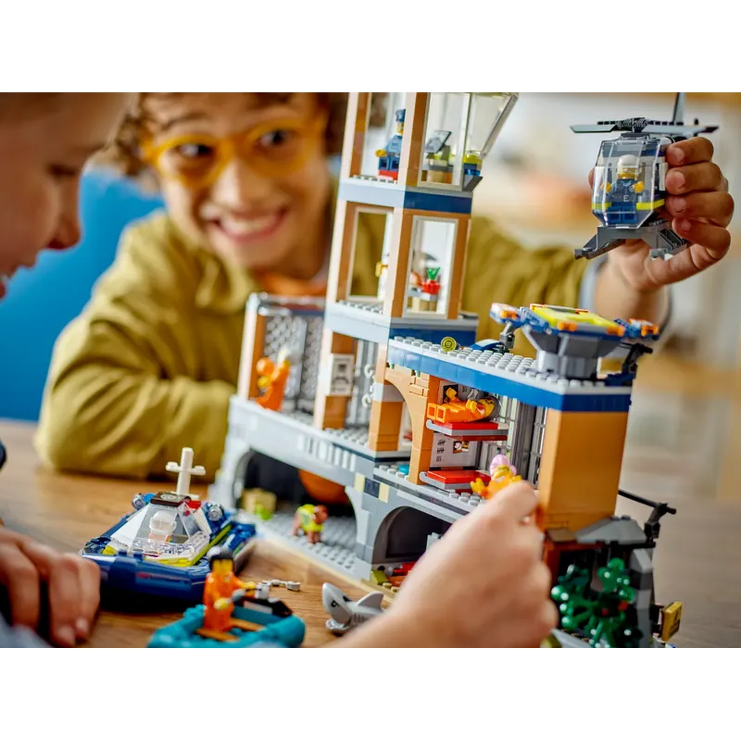 Des enfants jouent avec un jeu Lego. Un hélicoptère, un bateau et un bâtiment sont visibles. Un enfant tient l'hélicoptère, l'autre joue avec le bâtiment.