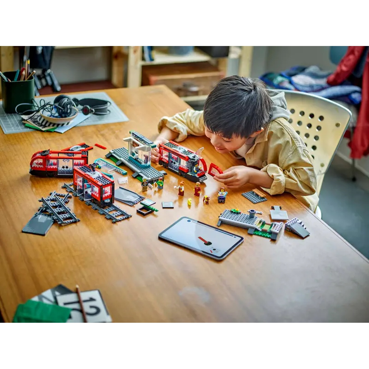 A child is playing with a toy train set on a wooden table. The set includes a train, tracks, and miniature figures.