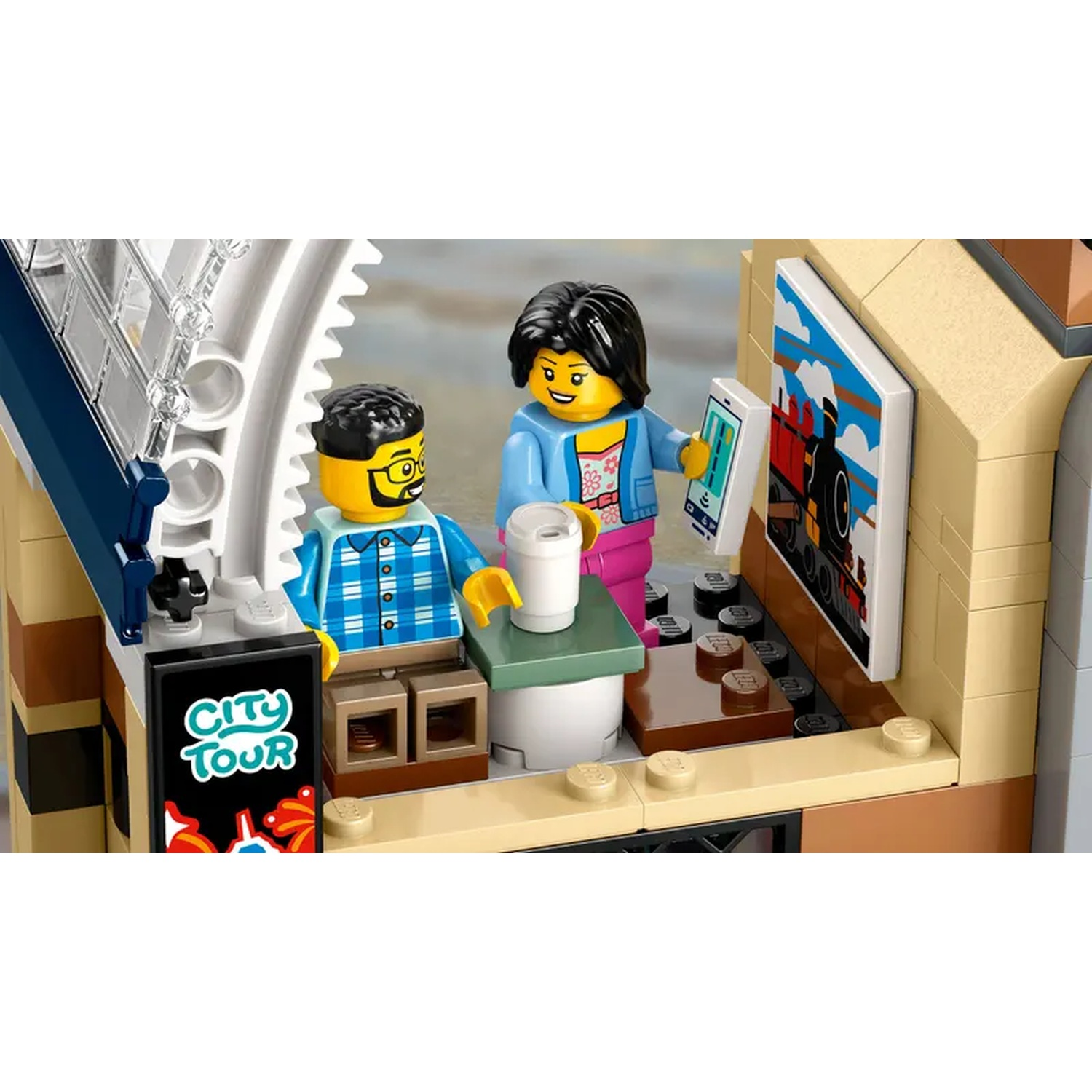 Lego-scène: twee figuren, een man en een vrouw, bij een 'City Tour'-stand. Er is een schilderij van een trein aan de muur en een koffiekopje.
