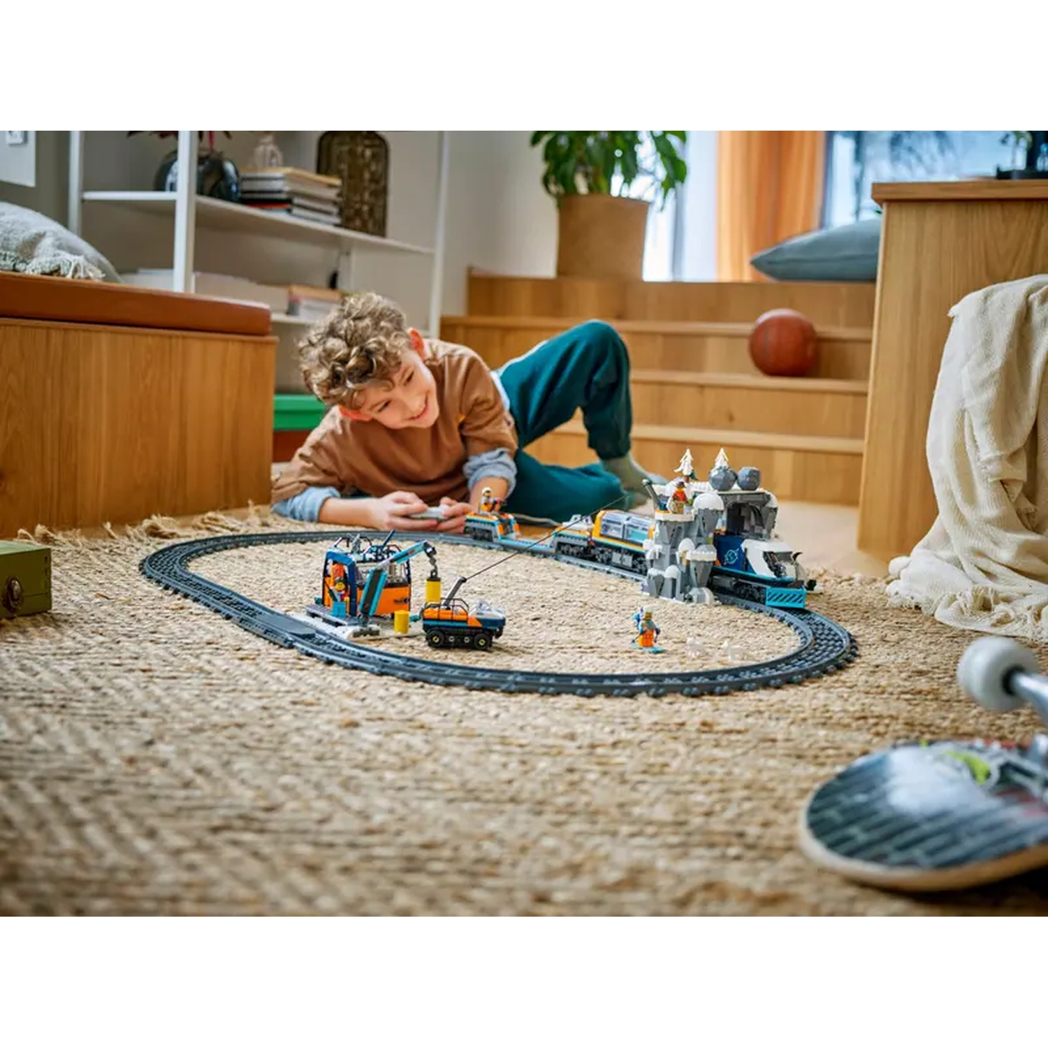 A boy plays with a toy train set. The track is on a rug. The train has a blue and orange color scheme and is on a brown background.