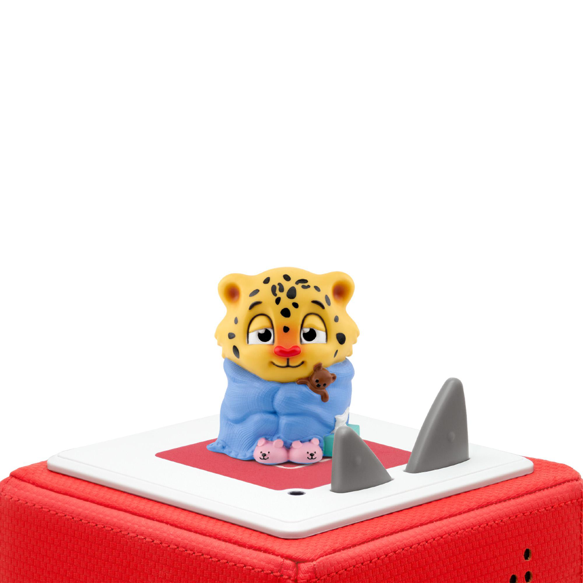 Ein Spielzeugleopard mit Decke und Teddybär auf einer roten Box mit weißer Oberseite und grauen Flossen.