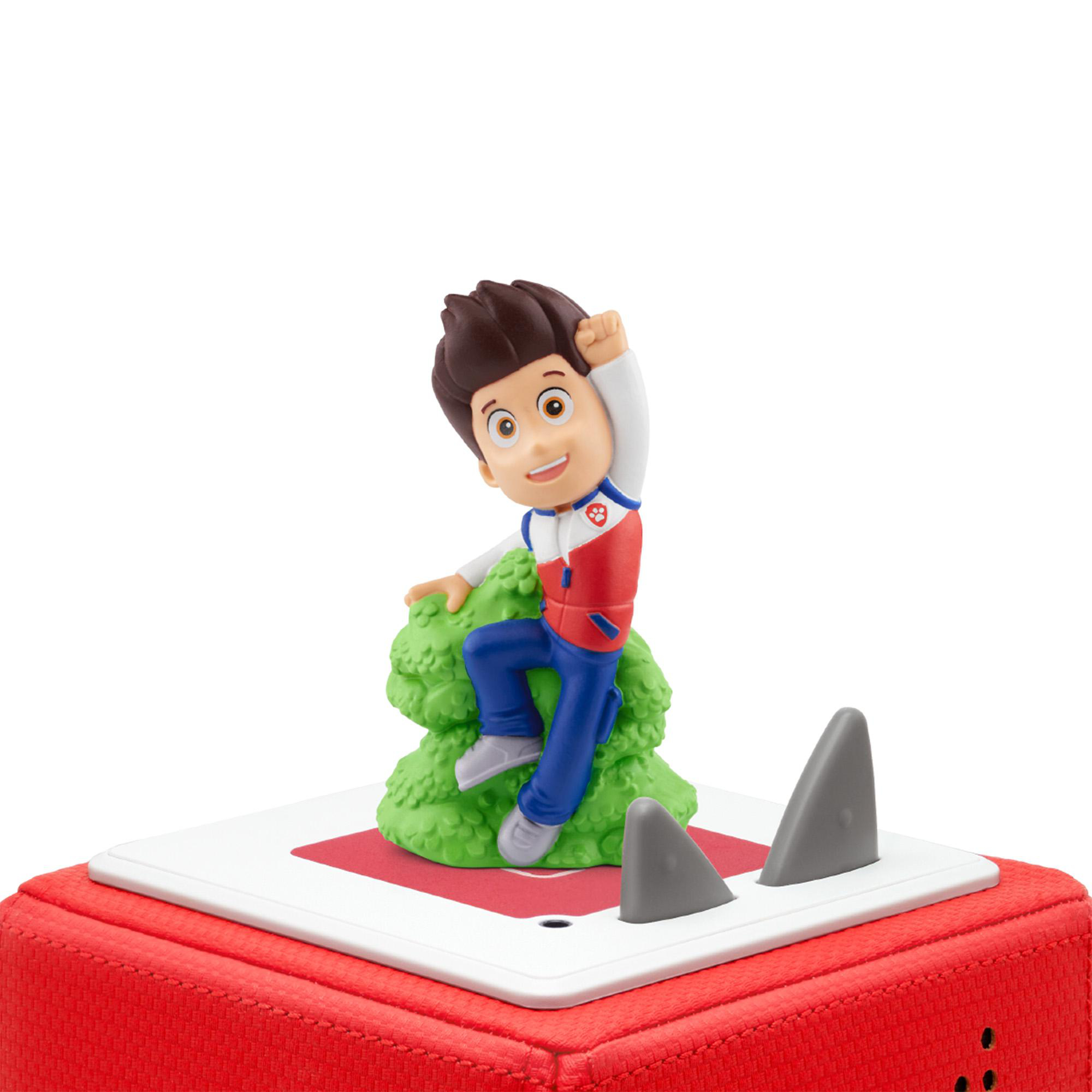 Eine Paw Patrol-Figur klettert auf einen grünen Busch auf einer roten Box mit Haifischflossen. Die Figur trägt Rot und Blau.