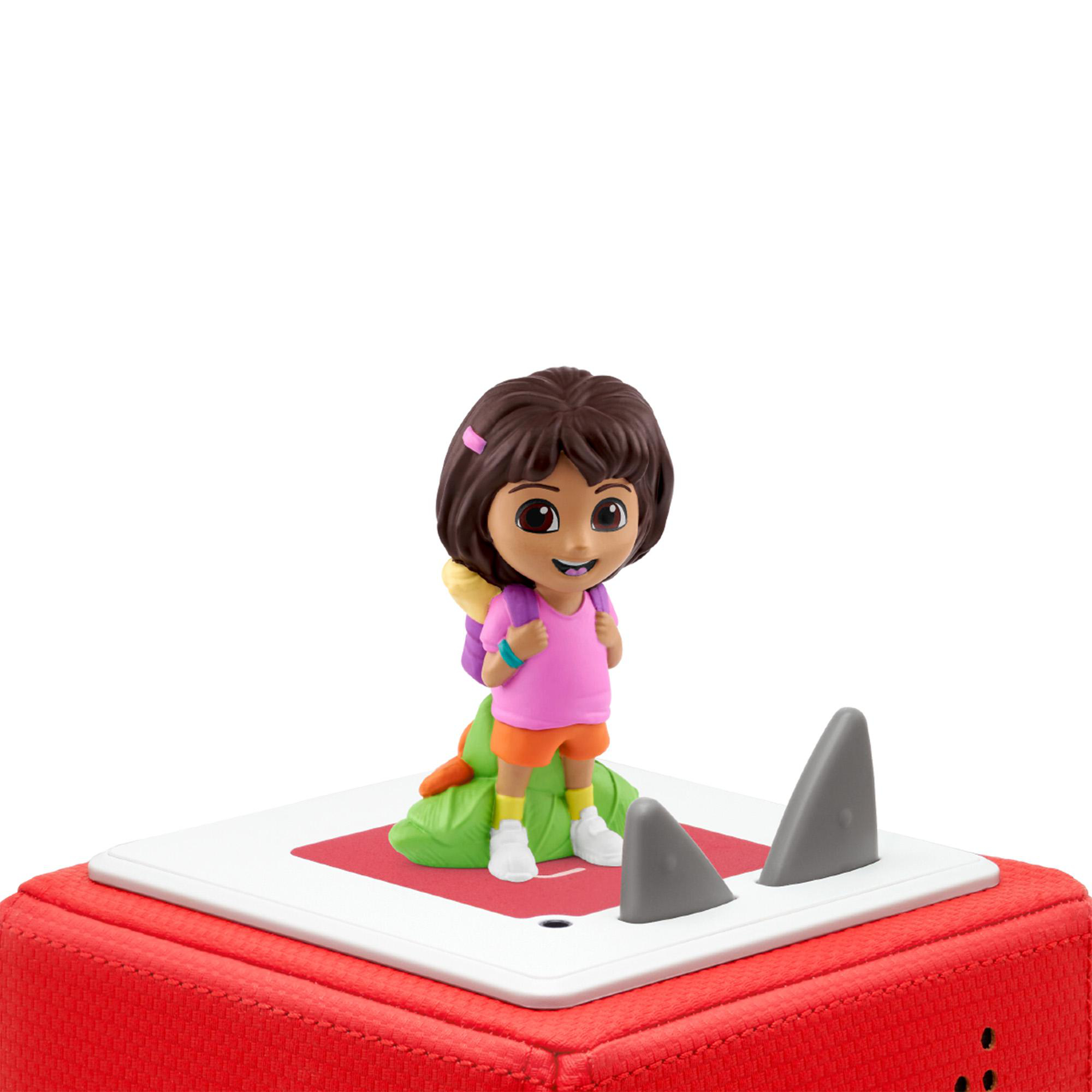 Dora-Figur auf einer rot-weißen Oberfläche mit grauen Haifischflossen. Sie trägt ein rosa Hemd, orange Shorts und weiße Schuhe.