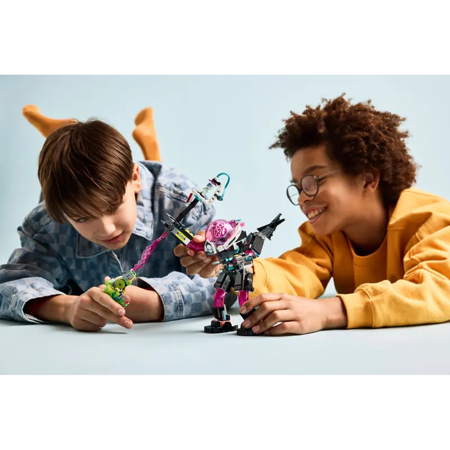 Twee kinderen spelen met robotspeelgoed. Eén schiet een paarse straal. De ander glimlacht. Blauwe en gele kleding zijn zichtbaar.