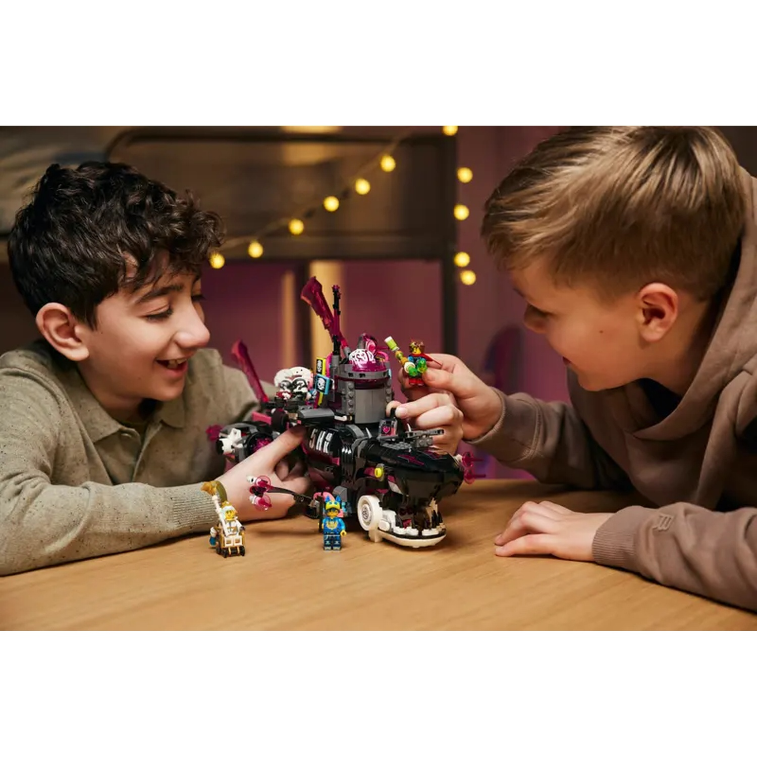 Twee jongens spelen met een Lego-set op een houten tafel. De Lego-set is zwart en roze met verschillende minifiguren.
