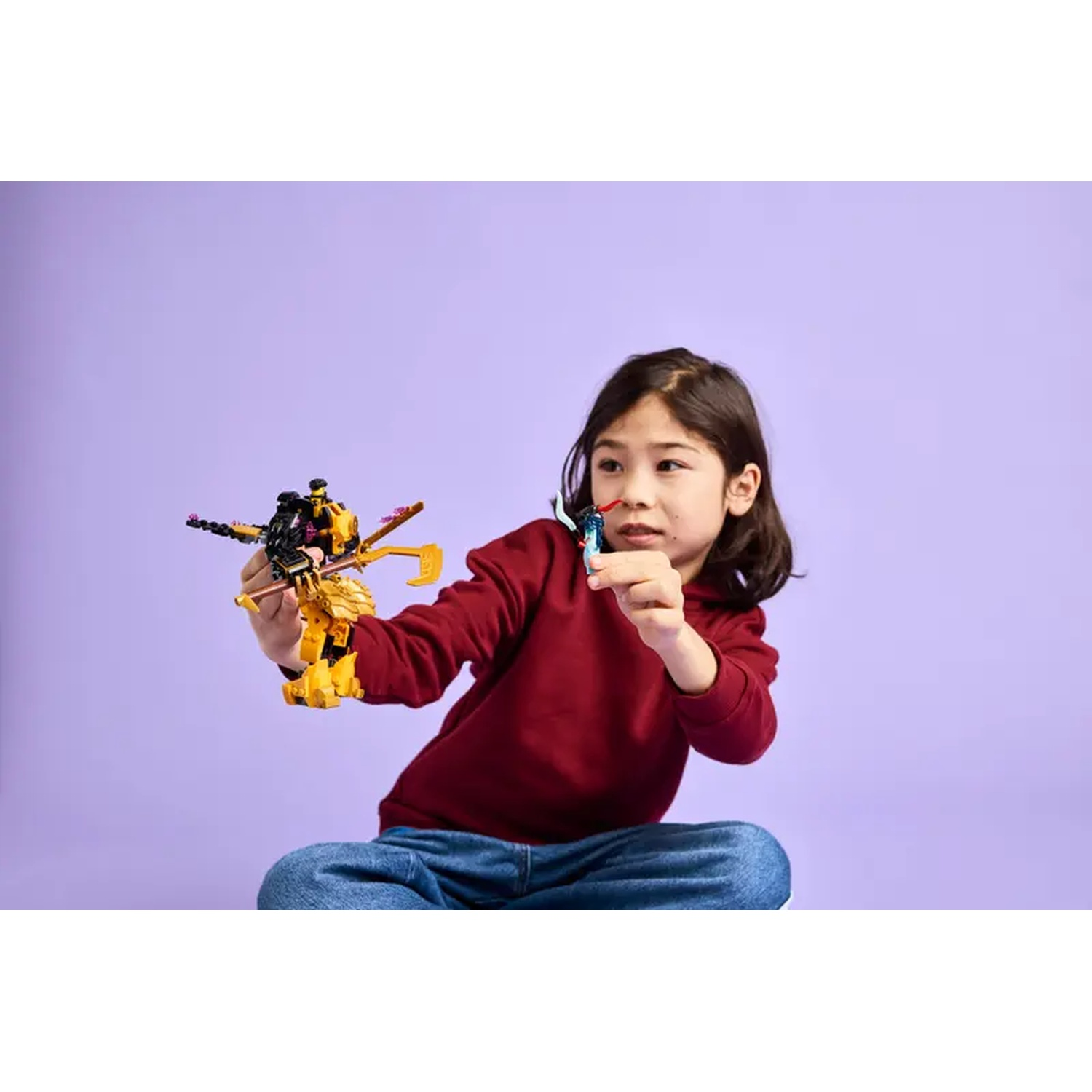A child in a red hoodie holds two toy figures against a purple background. One figure is yellow, the other blue.