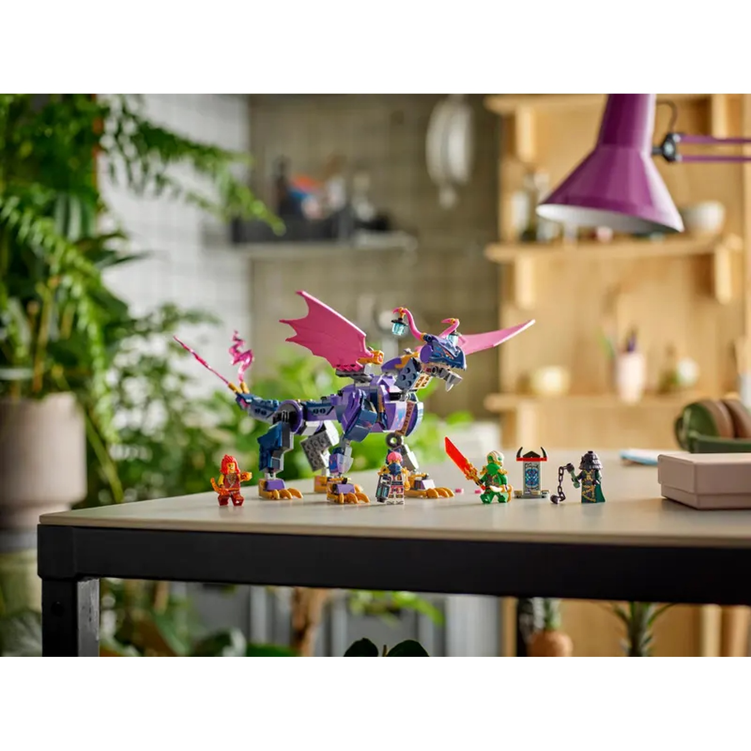 Een Lego-set met een paarse draak met roze vleugels en verschillende minifiguren op een tafel. Achtergrond bevat planten en planken.