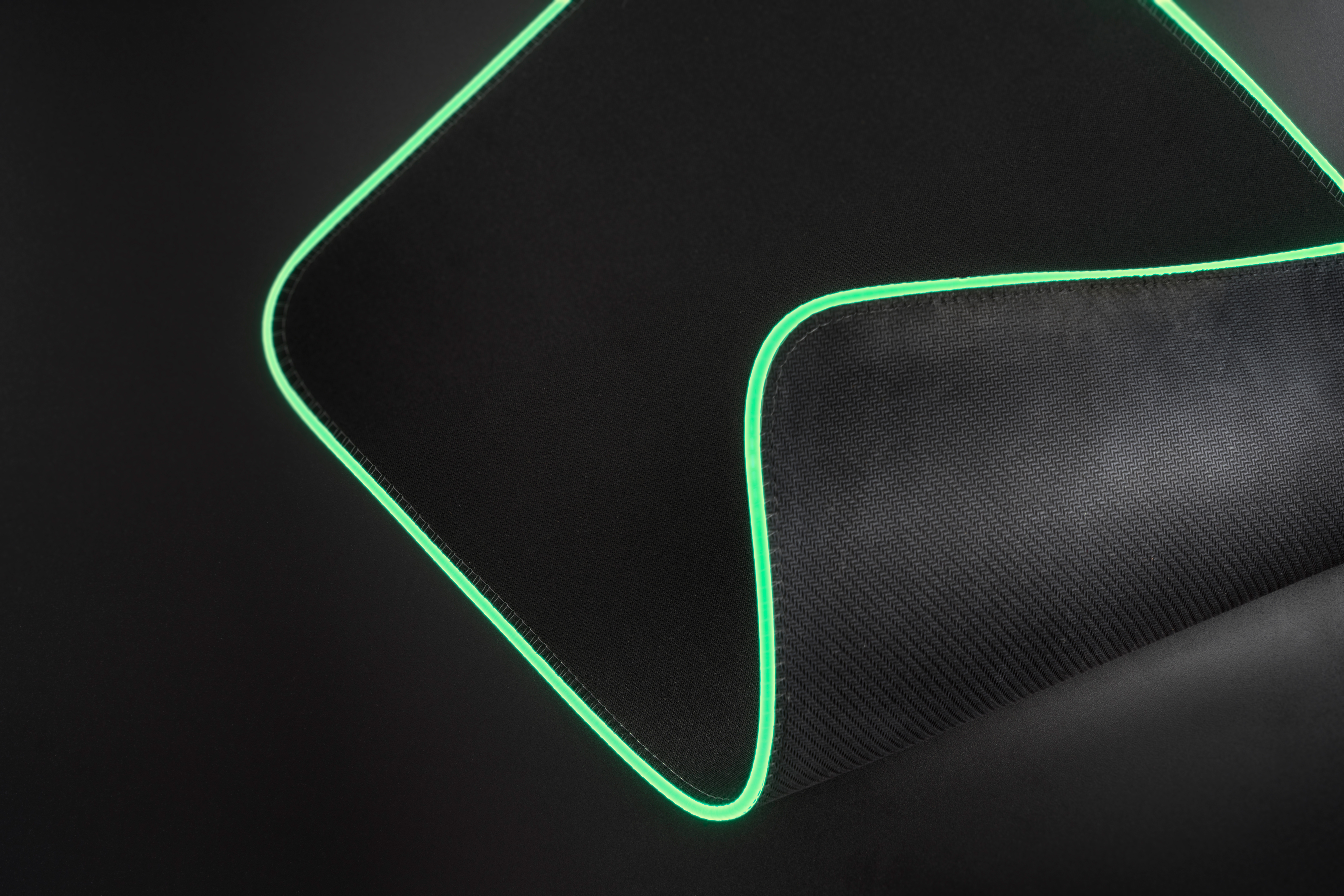 Czarna podkładka pod mysz dla graczy z zieloną świecącą krawędzią. Powierzchnia jest teksturowana. Tło jest ciemne.