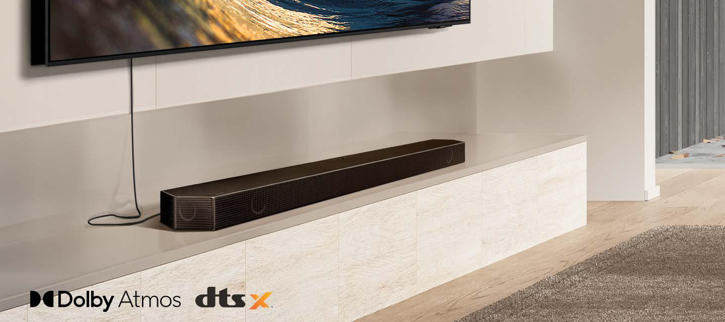 Eine schwarze Soundbar steht auf einem Regal unter einem Fernseher. Das Regal befindet sich über einem weißen Schrank.