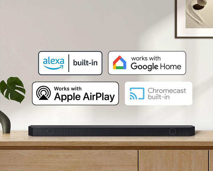 Eine schwarze Soundbar steht auf einer Holzoberfläche. Darüber befinden sich Logos für Alexa, Google Home, Apple AirPlay und Chromecast.