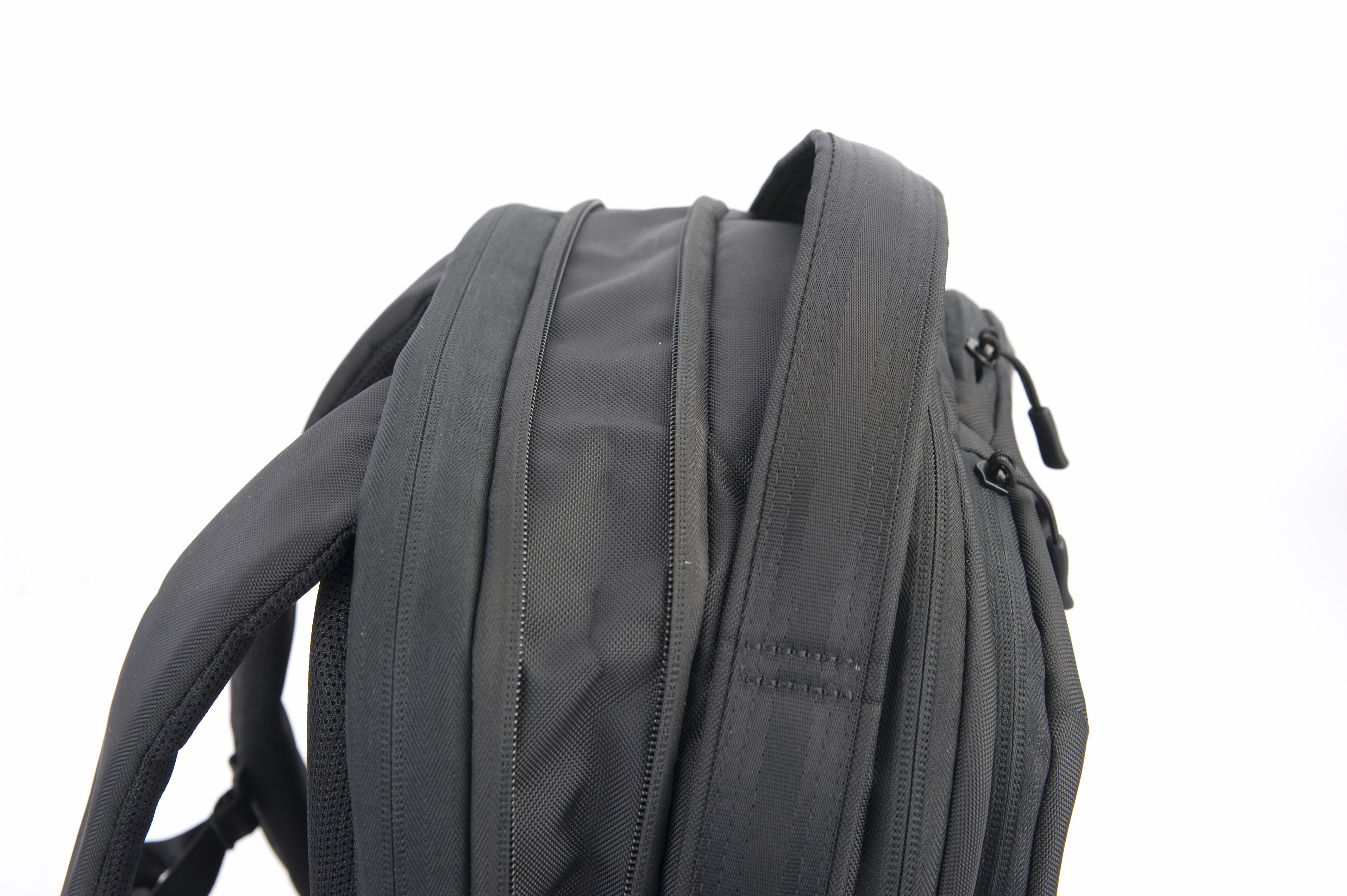 Zbliżenie czarnego plecaka na białym tle. Widoczne paski, zamki błyskawiczne i teksturowana tkanina.