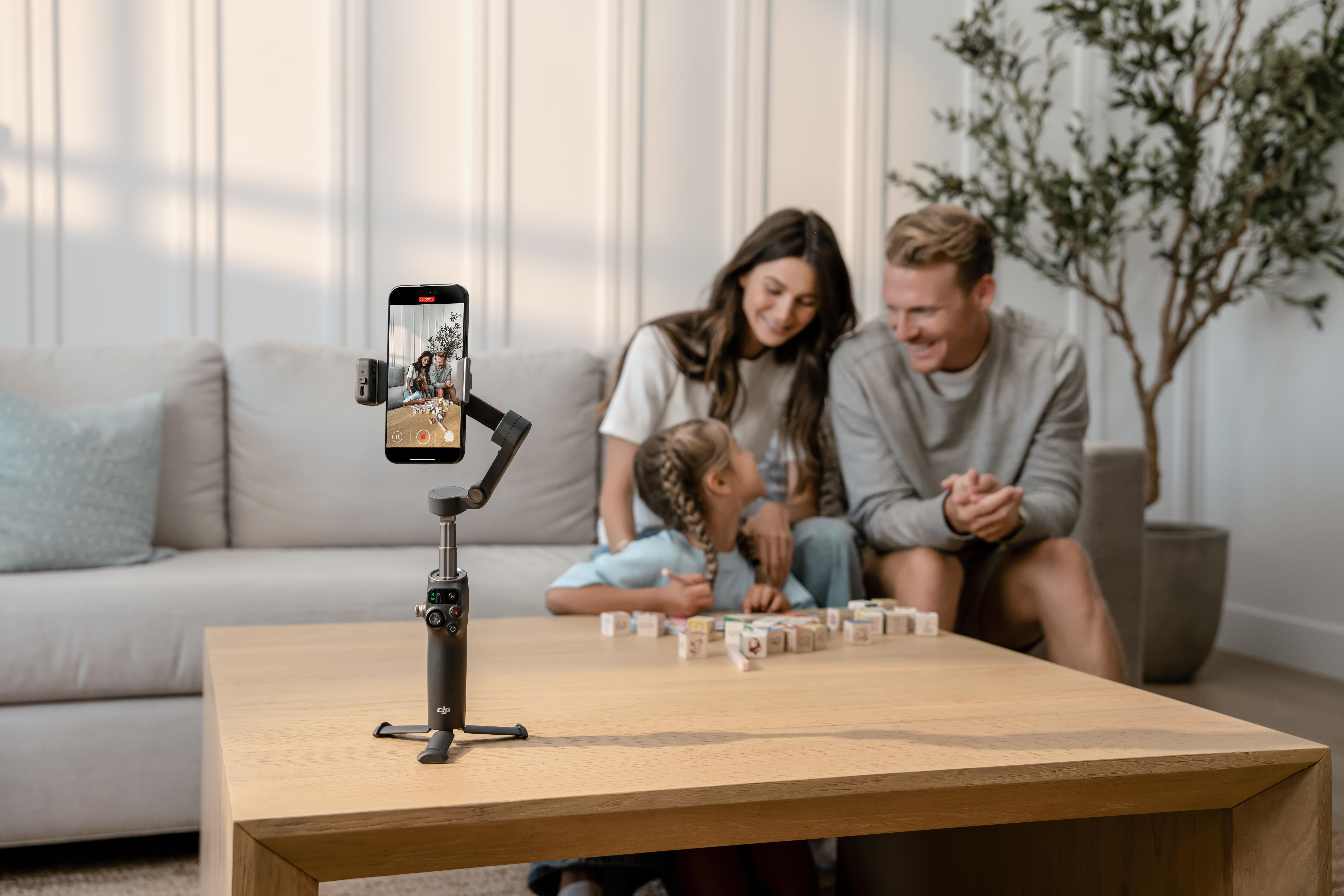 Familie nimmt Video auf. Ein Telefon auf einem Gimbal, Tisch, Sofa und Pflanze im Bild.