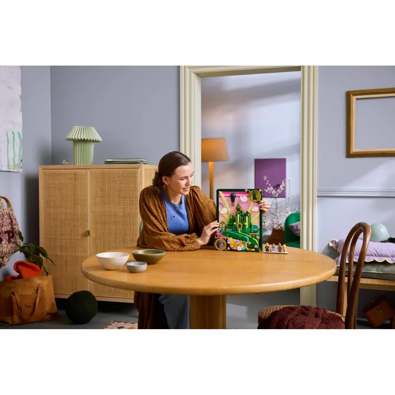Een vrouw zit aan een ronde tafel met een kleurrijke doos met een speelgoed bouwset in een kamer met een kast en een houten stoel.