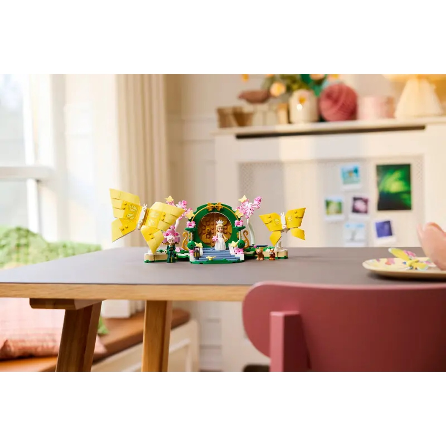 Een Lego-set op een tafel met gele vleugels. Een roze stoel op de voorgrond. Een witte kast en een raam op de achtergrond.
