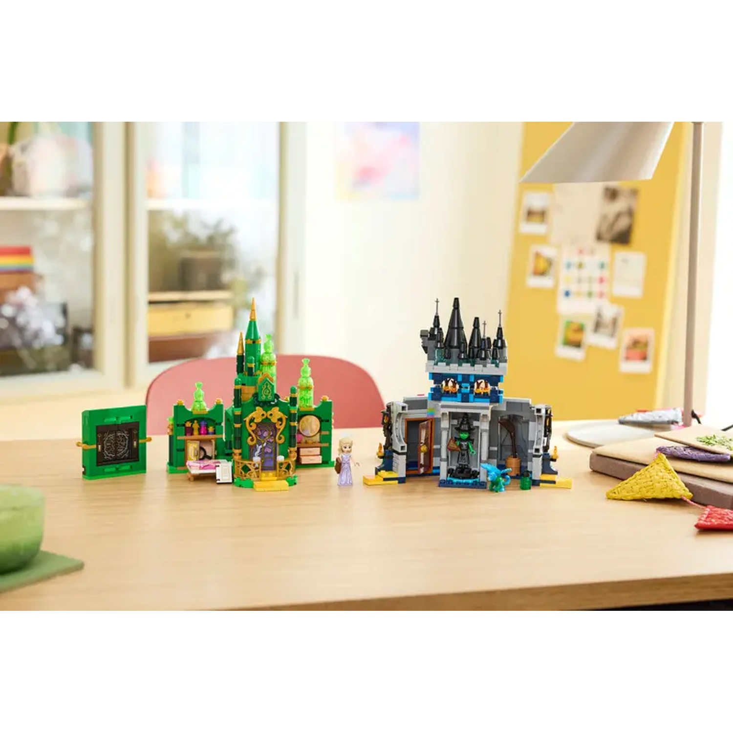 Une table présente des châteaux et des figurines LEGO. L'un est vert, l'autre gris. L'arrière-plan comprend une chaise rouge, une fenêtre et des post-it jaunes.