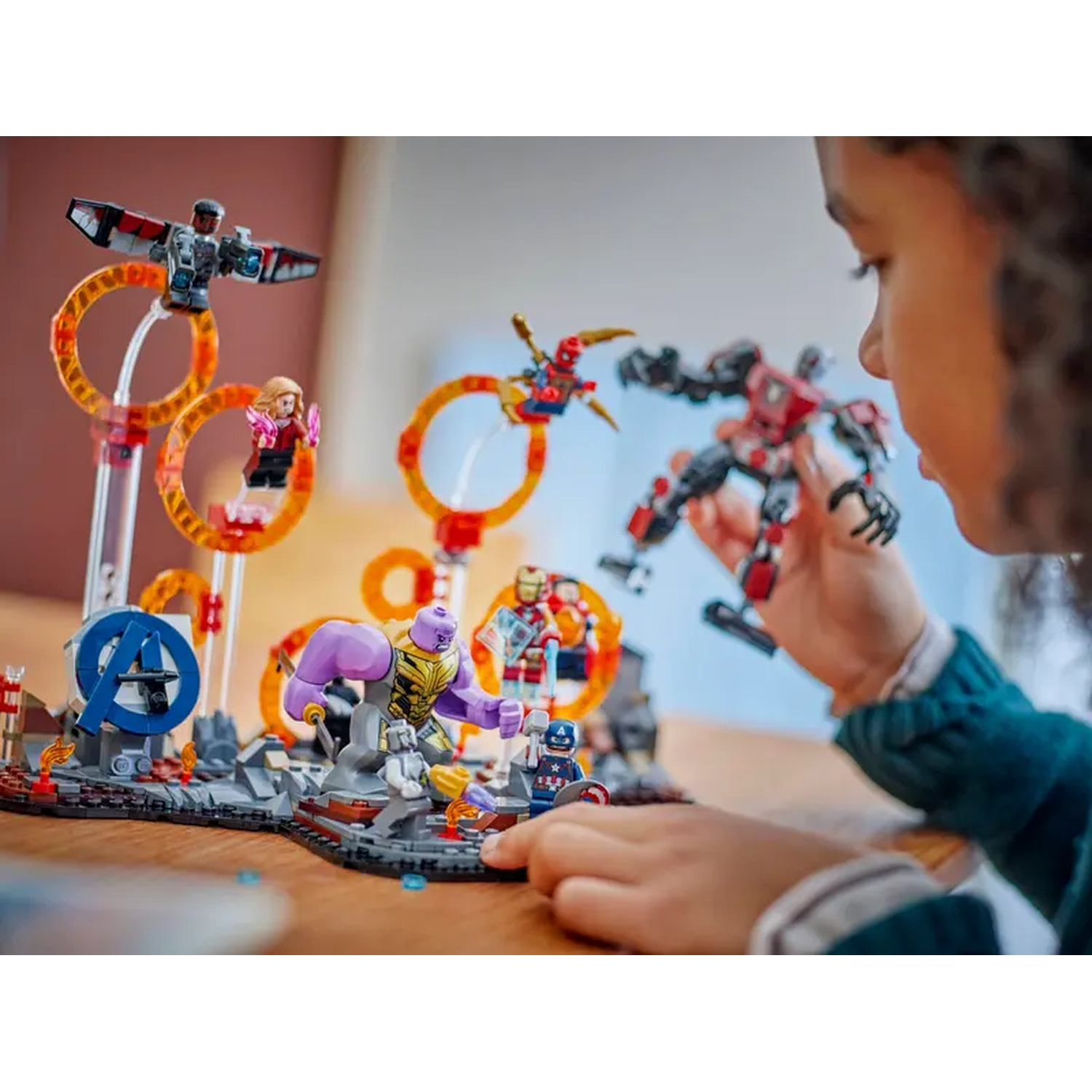 A child plays with Lego Marvel figures, including Iron Man, Captain America, and Thanos, with a backdrop of an Avengers scene.