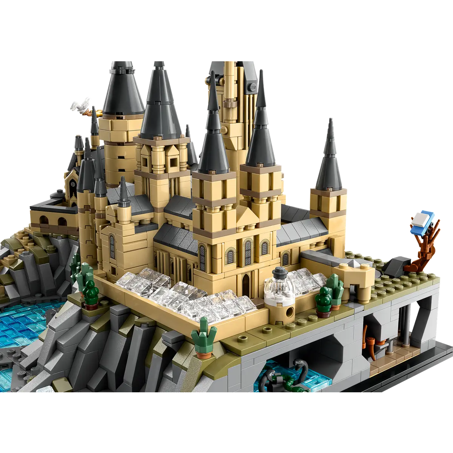 Lego model of Hogwarts castle with tan and black towers. Includes a lake, rocky terrain, and small green trees.