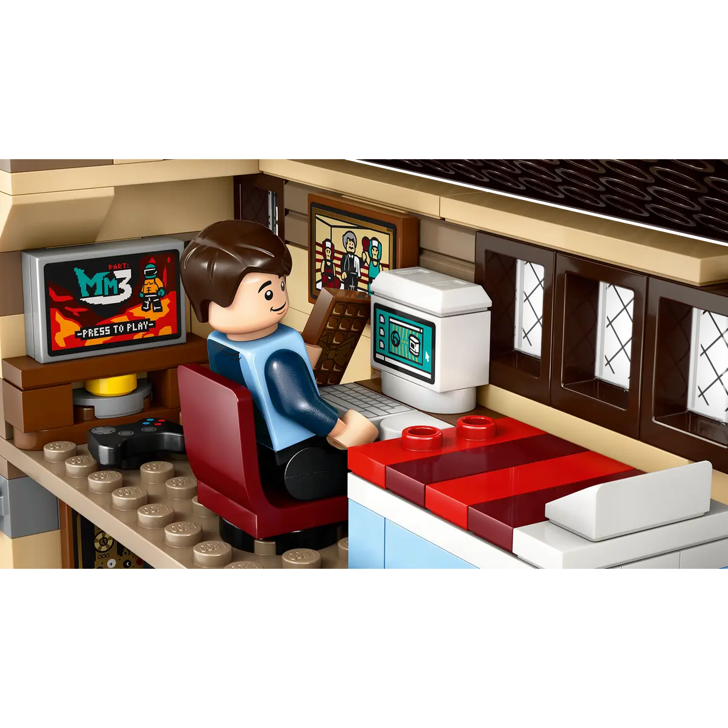 Lego scene of a person sitting at a desk with a computer and game console. A TV displays a game. Red chair.