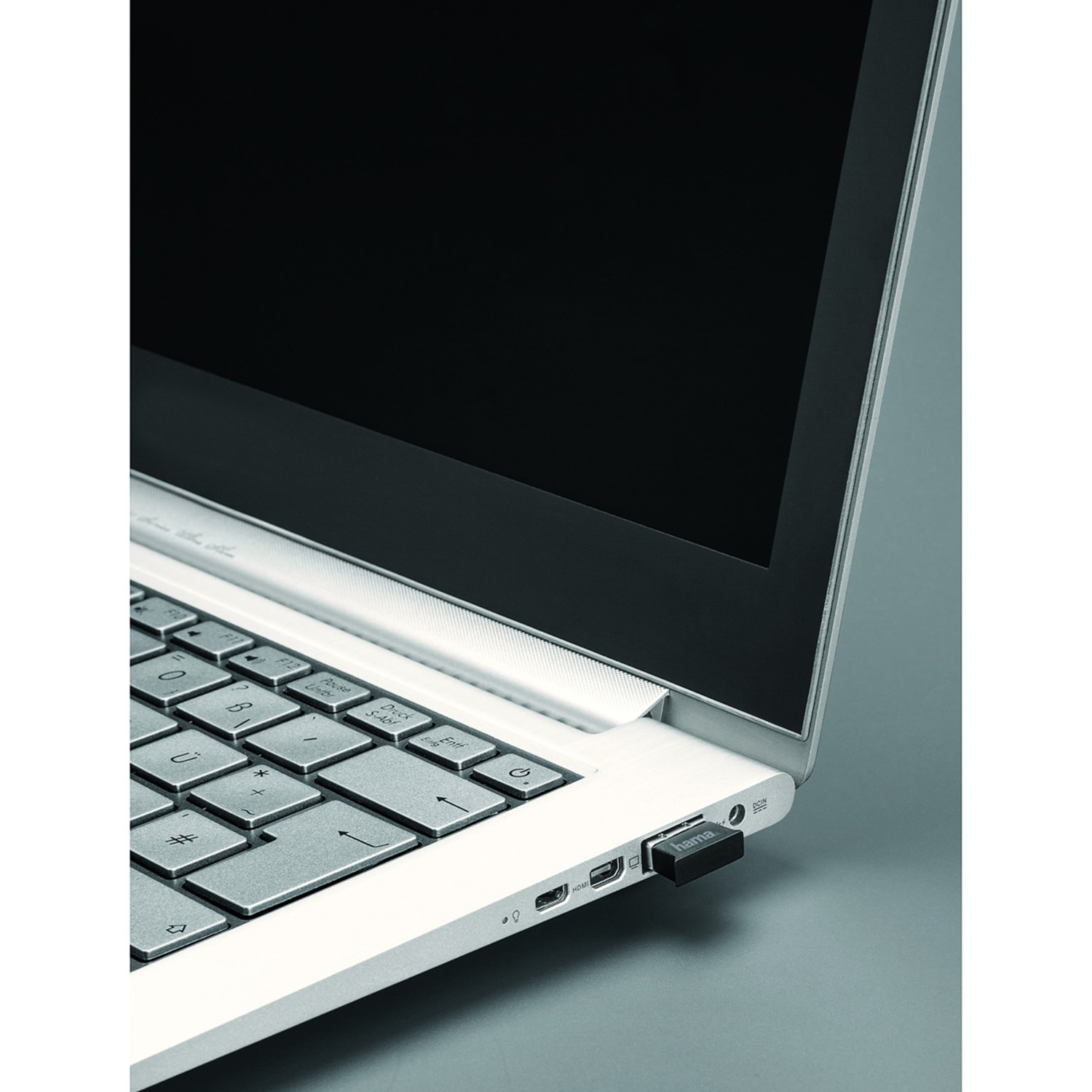 Un laptop con schermo nero ha un'unità USB nera inserita. La tastiera è bianca e lo sfondo è grigio.
